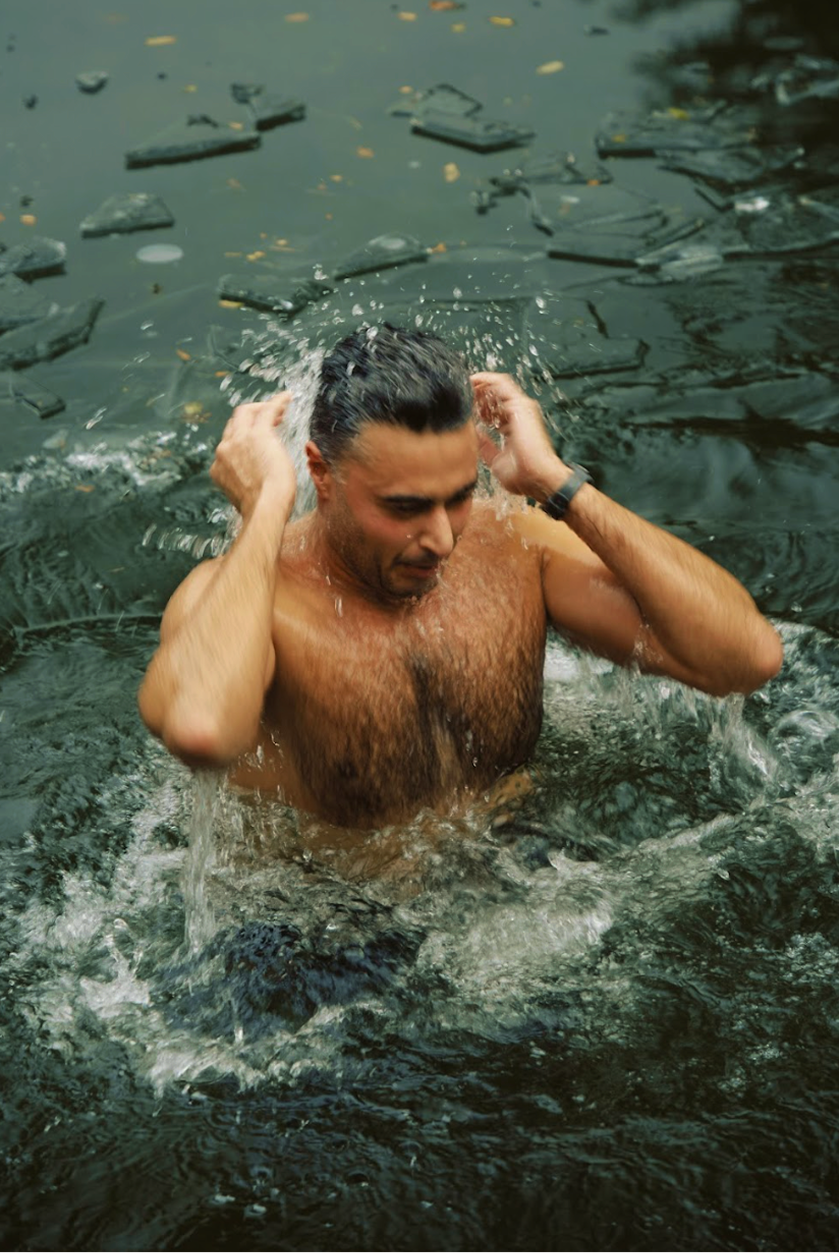 Group of five people enjoying a baptism in an outdoor pool surrounded by trees, with a woman in the center praying and smiling.