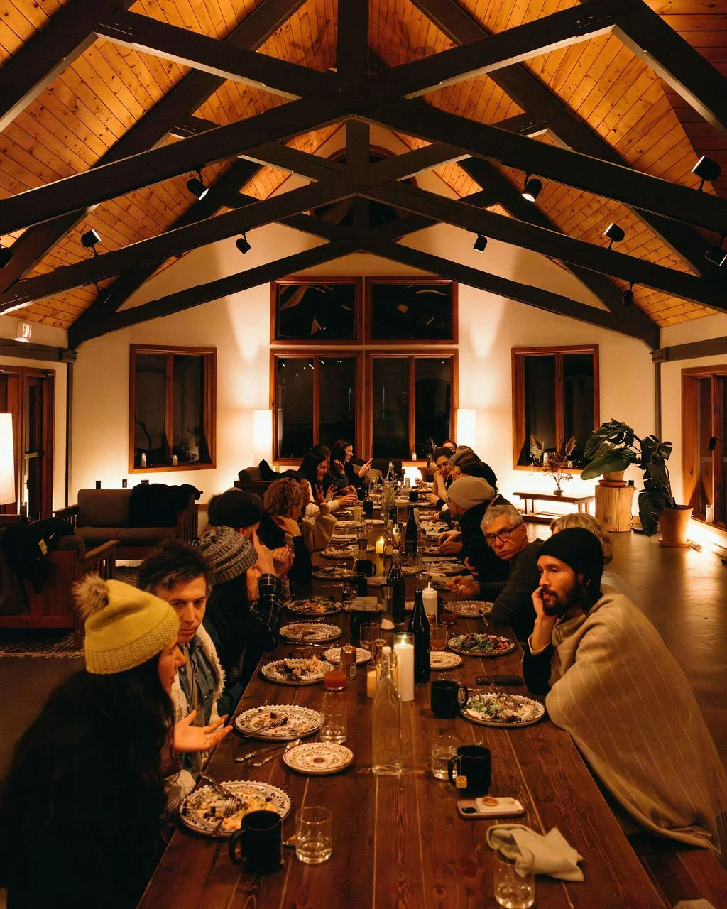 A long dining table set for a meal with candles, floral centerpieces, plates with food, and glasses in a dimly lit room.