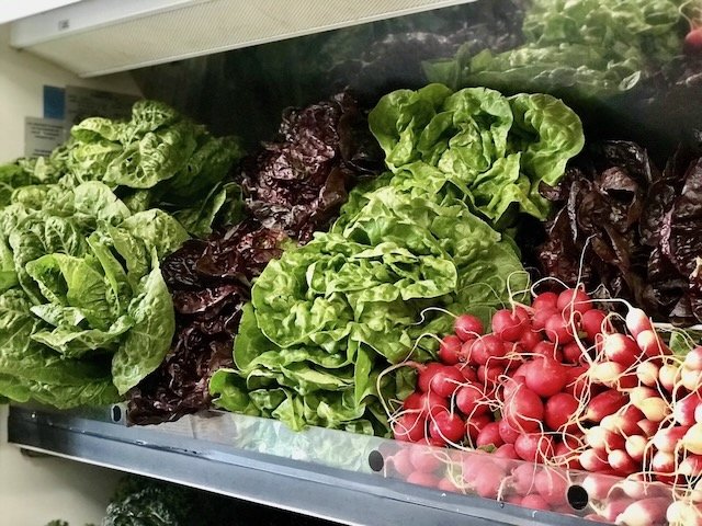 Fresh leafy greens and radishes on display in a grocery store produce section.