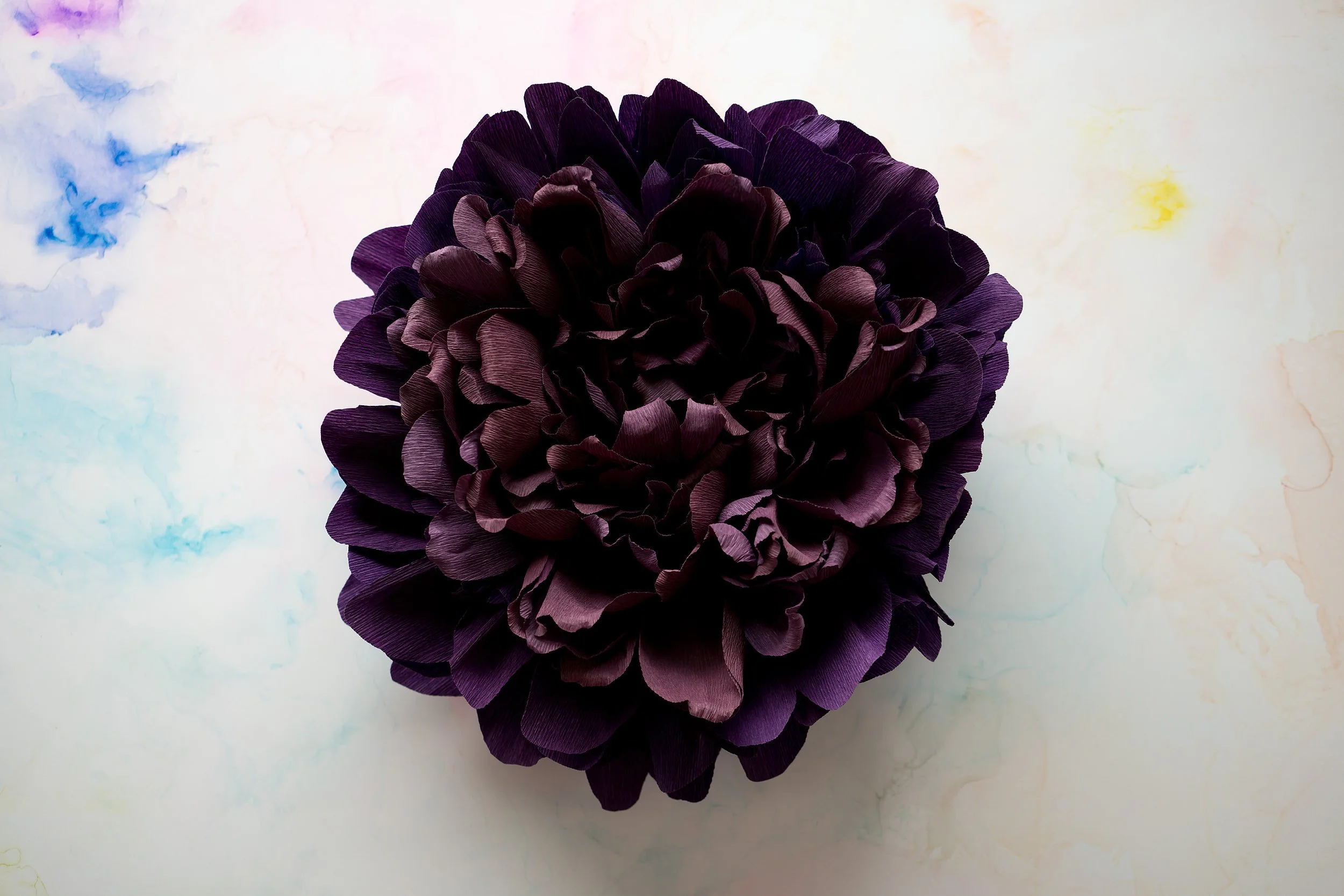 A dark purple artificial flower with multiple layered petals on a light marble surface.