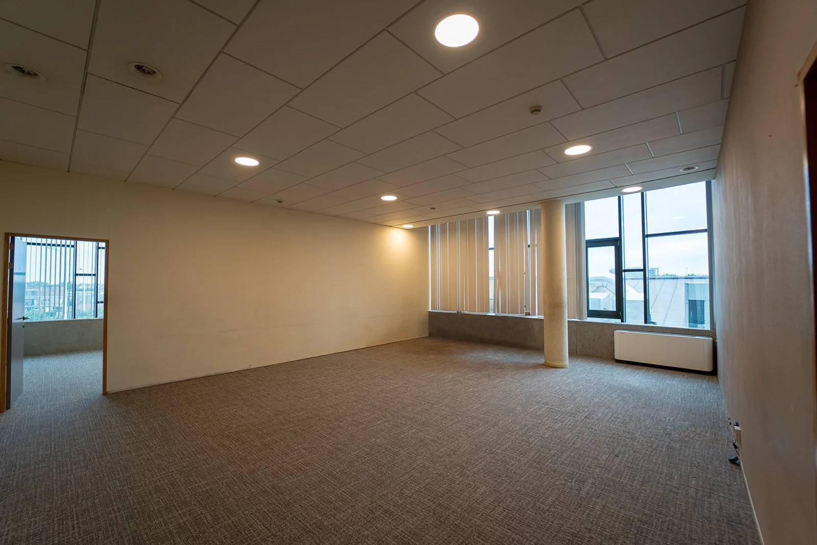 Bovenaanzicht van een wit appartementencomplex met meerdere verdiepingen en balkons, met een blauwe lucht en wolken op de achtergrond, en een tuin met bankjes op de voorgrond, vertigo oostende, vertigo, appartement oostende, appartement te koop