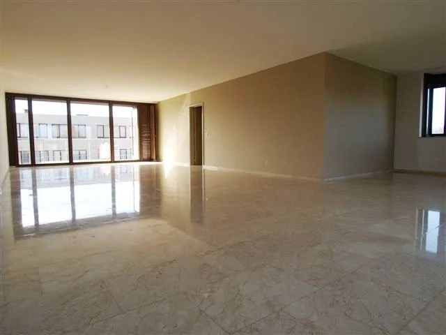 Leeg appartement met grote ramen en marmeren vloer.