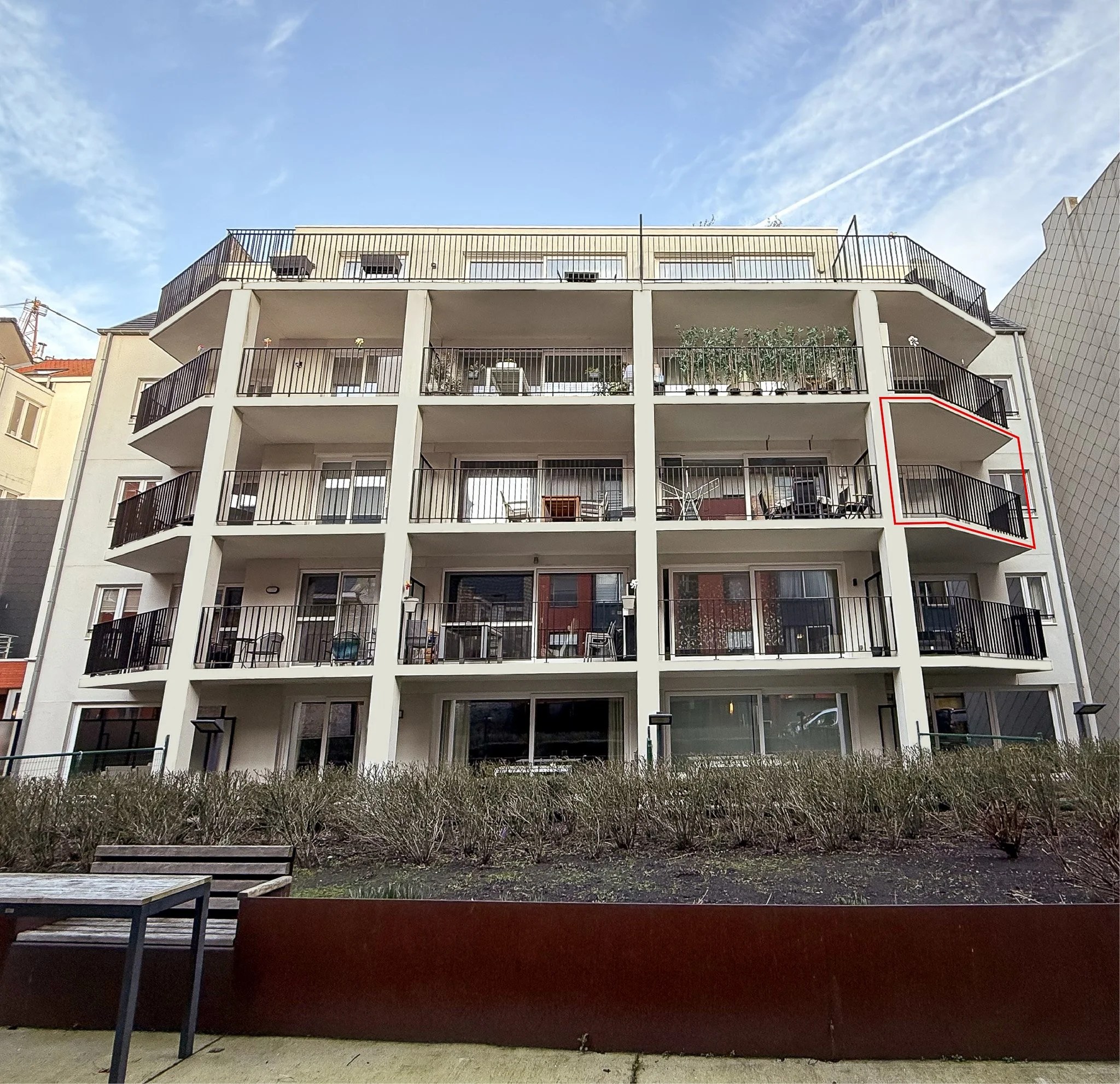 Een wit appartementencomplex met meerdere verdiepingen en balkons. Een balkon aan de rechterkant is gemarkeerd met een rood kader, appartement vertigo te koop, appartement oostende te koop