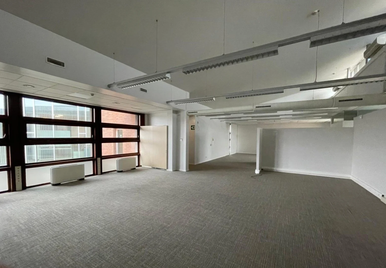 Vier verdiepingen hoog modern appartementencomplex met glazen balustrades, een onderbouw met een garage en een inrit, een auto geparkeerd voor het gebouw, en een teken dat de woning te koop is.