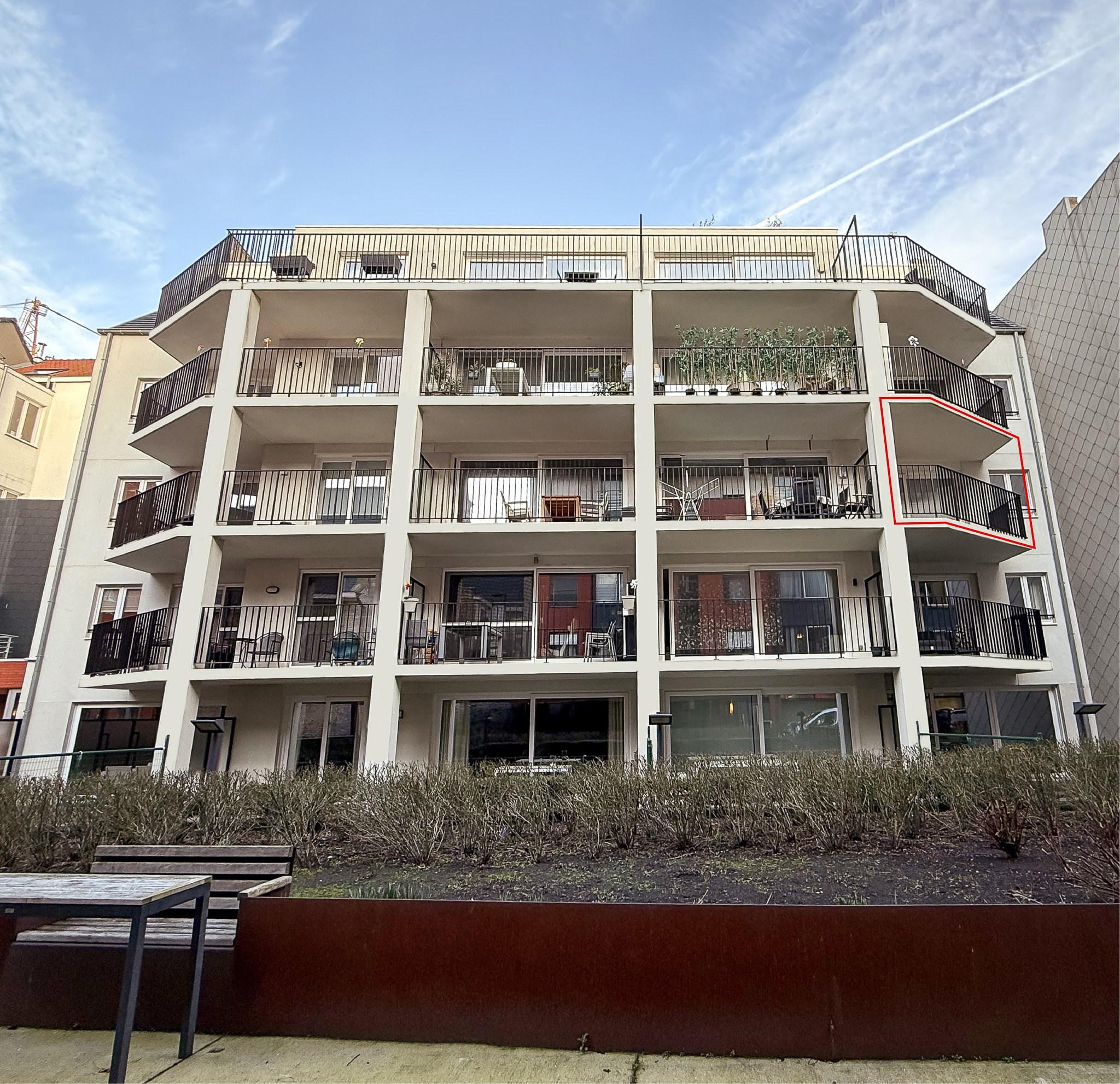 Een wit appartementencomplex met meerdere verdiepingen en balkons met zwarte relingen. Een balkon aan de rechterkant is gemarkeerd met een rood kader, vertigo oostende, vertigo, appartement oostende, appartement te koop