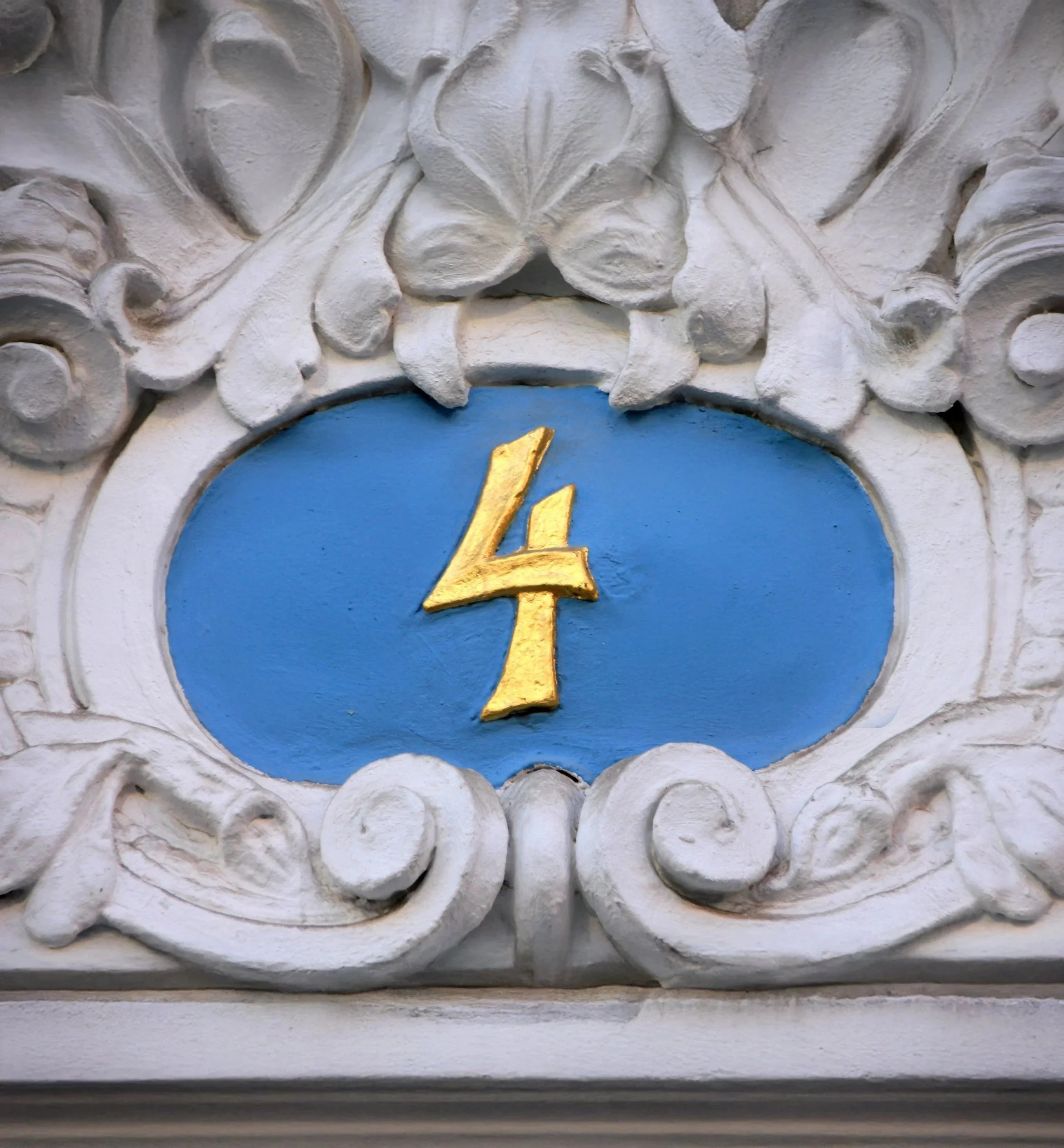 Ein kunstvoller Fassadenornament mit weißen Steinreliefs, im Zentrum ein blauer Kreis mit einem goldfarbenen Ziffernblatt.