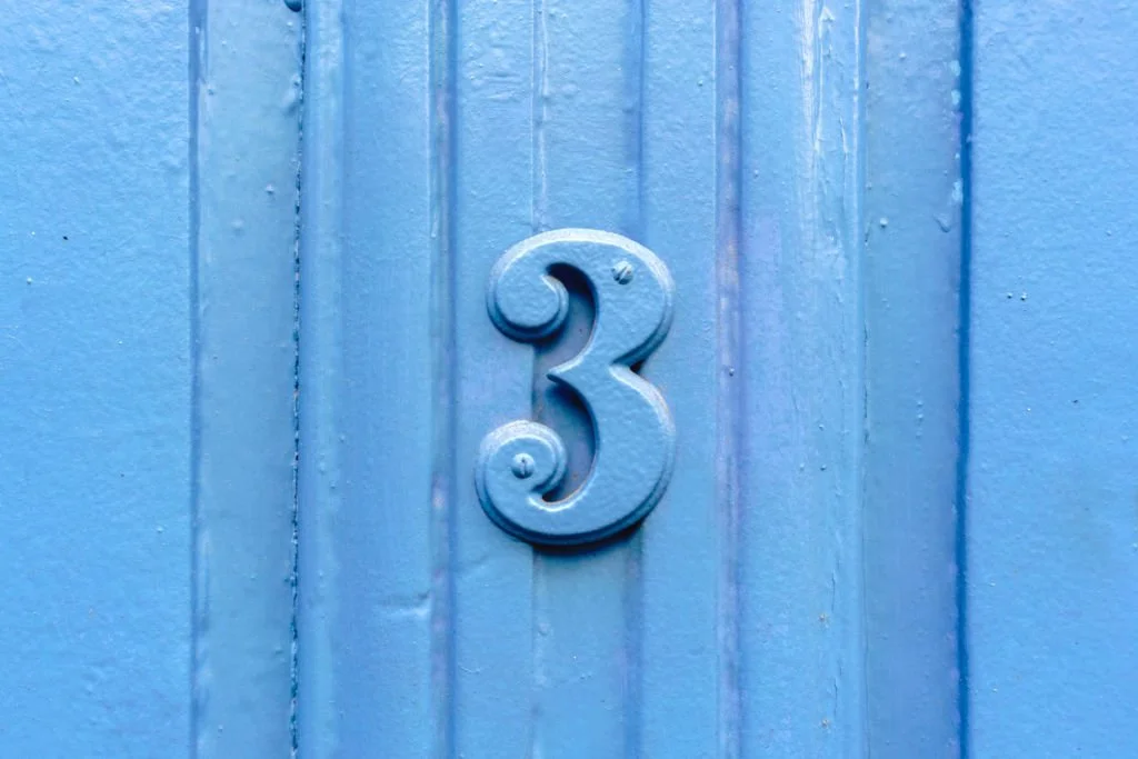 Hausnummer 3 an blauer Holzfassade.