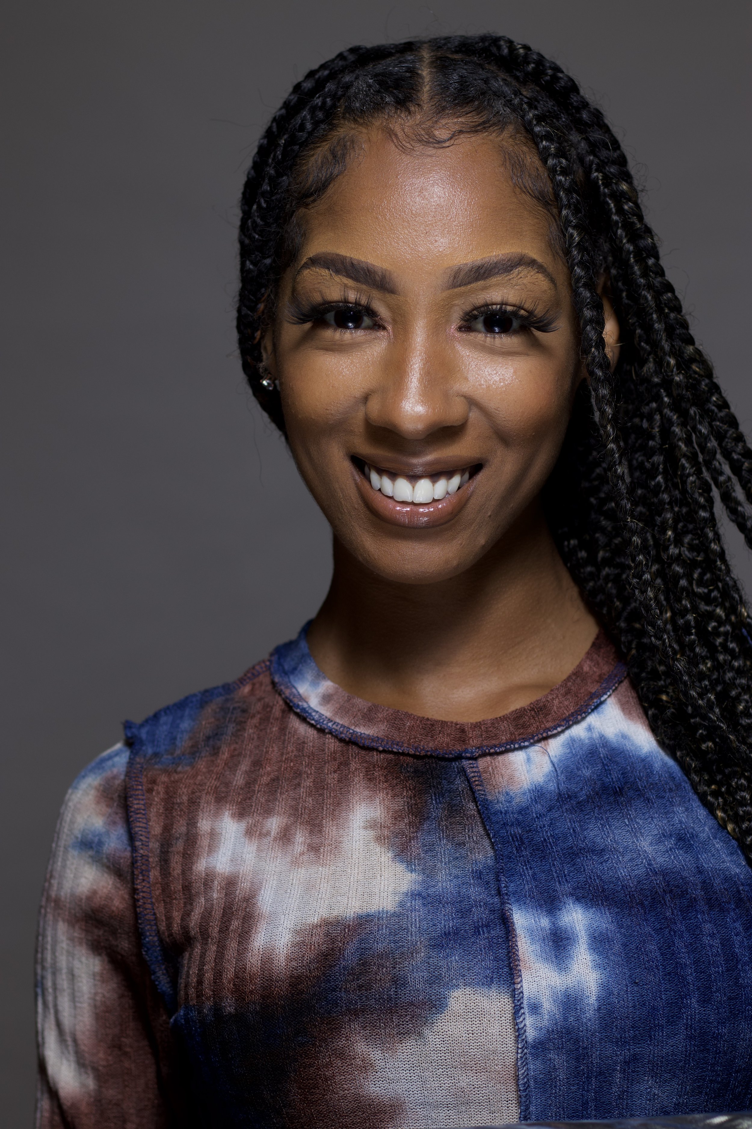 Tatiana Rawsstein, a woman, with braided hair smiling at the camera, wearing a tie-dye shirt in shades of blue and brown.