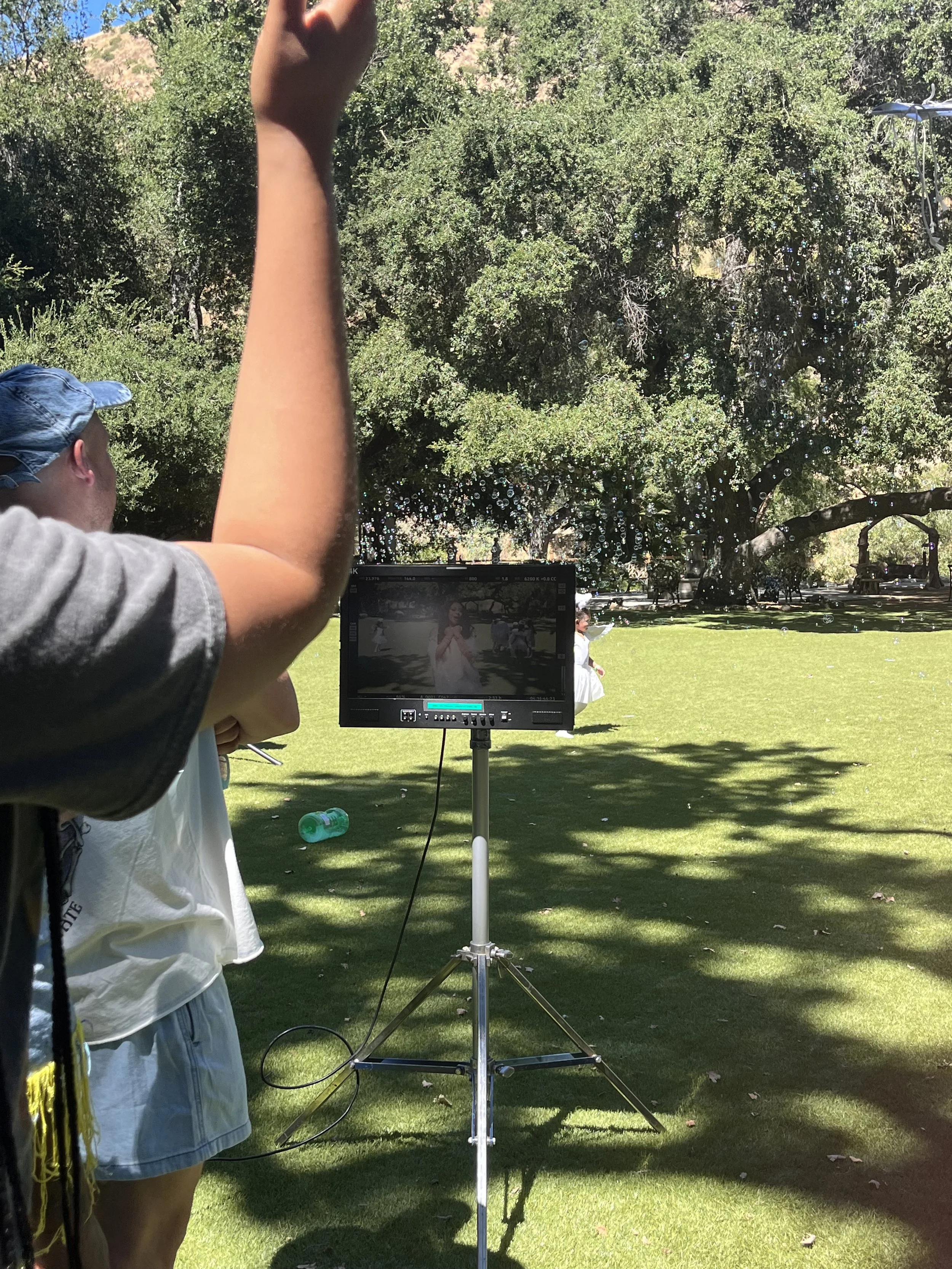 Outdoor film set with a monitor on a stand, trees in the background.
