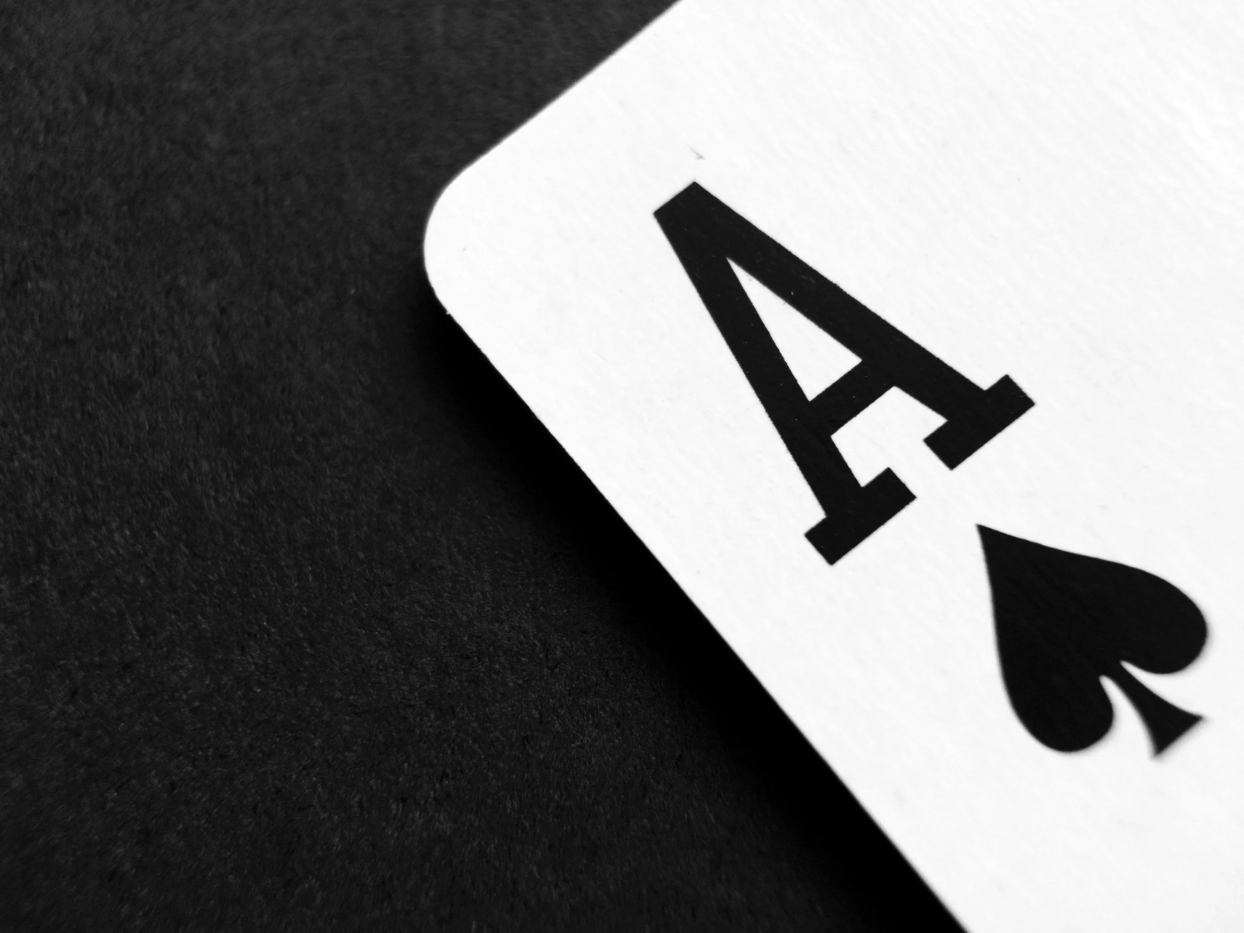 Close-up of a playing card, the Four of Spades, against a black background.