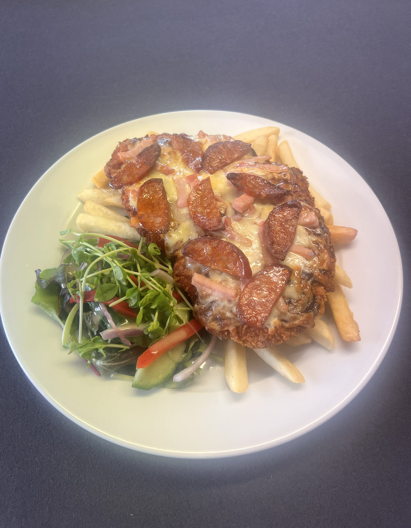 Plate with a serving of French fries, topped with melted cheese, tomato sauce, and meats, accompanied by a side salad with mixed greens and onion slices.