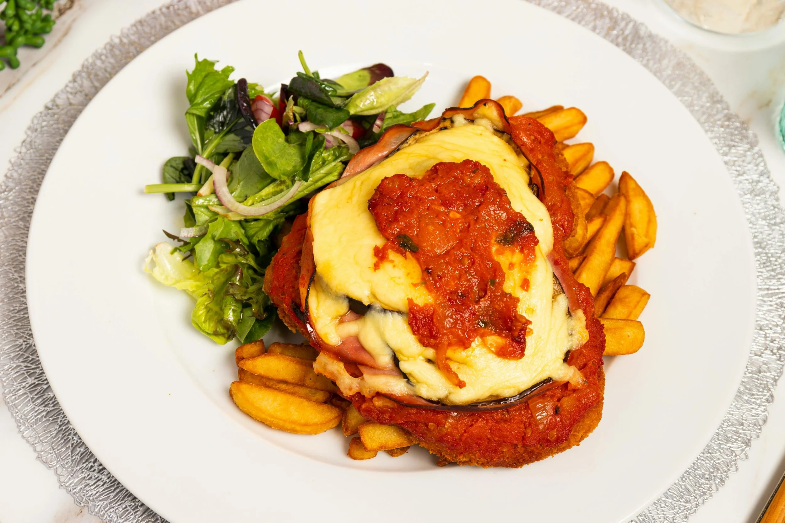 Plate with chicken parmesan topped with melted cheese and marinara sauce, served with French fries and a side salad with mixed greens and sliced onions.