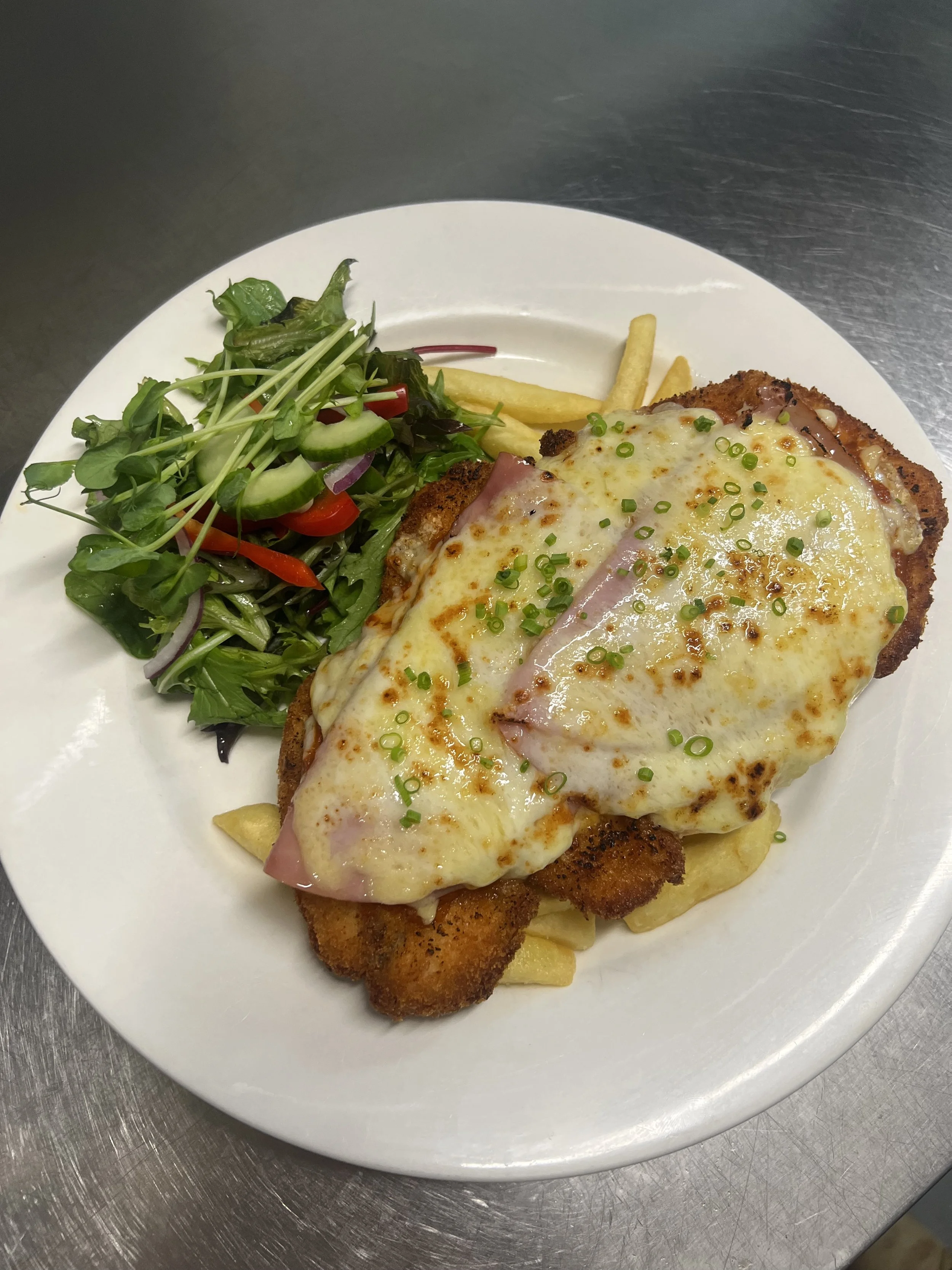 Plate with chicken parmesan topped with melted cheese and marinara sauce, served with French fries and a side salad with mixed greens and sliced onions.