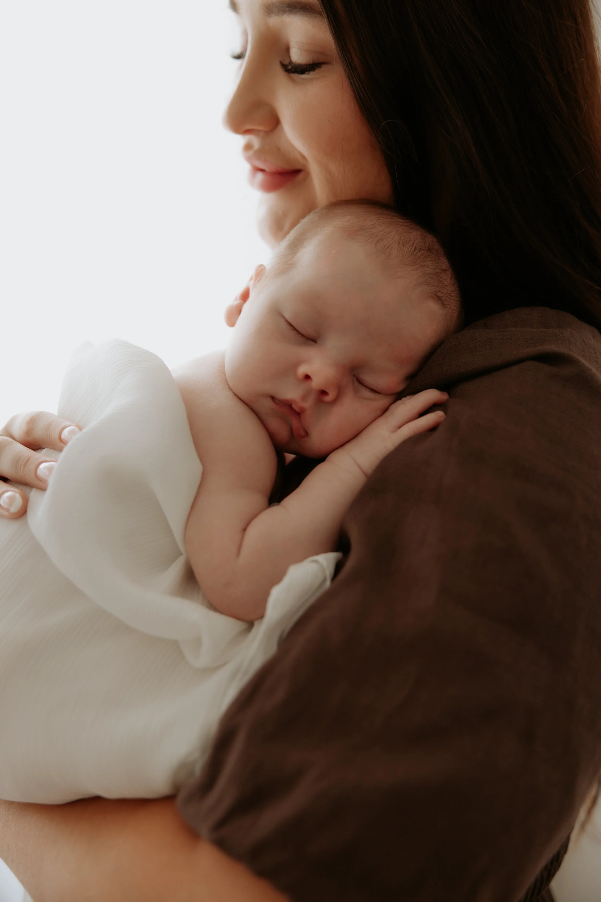 A woman holding a sleeping baby close to her chest, with her eyes closed and a gentle smile.