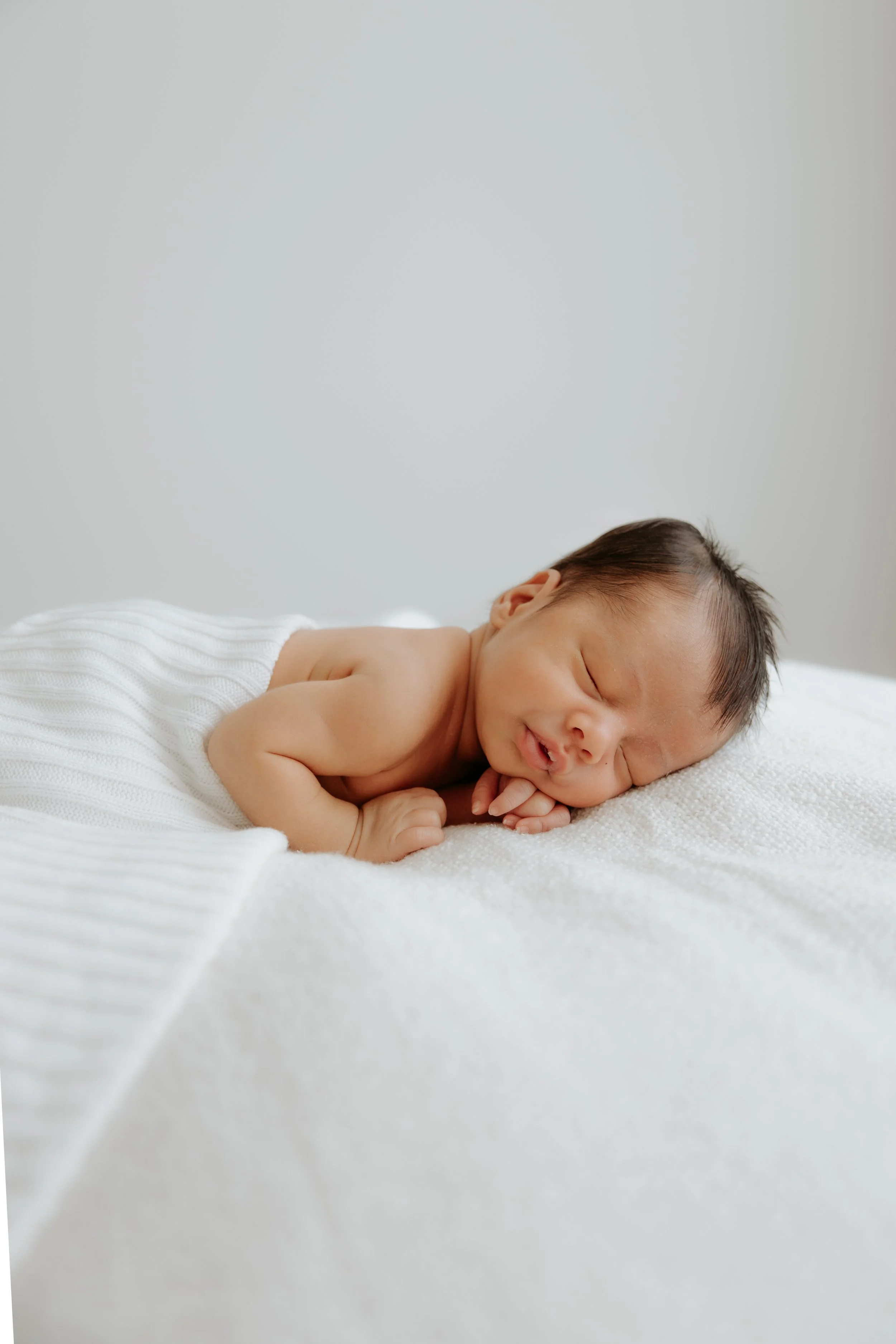 A sleeping newborn baby lying on a white blanket.