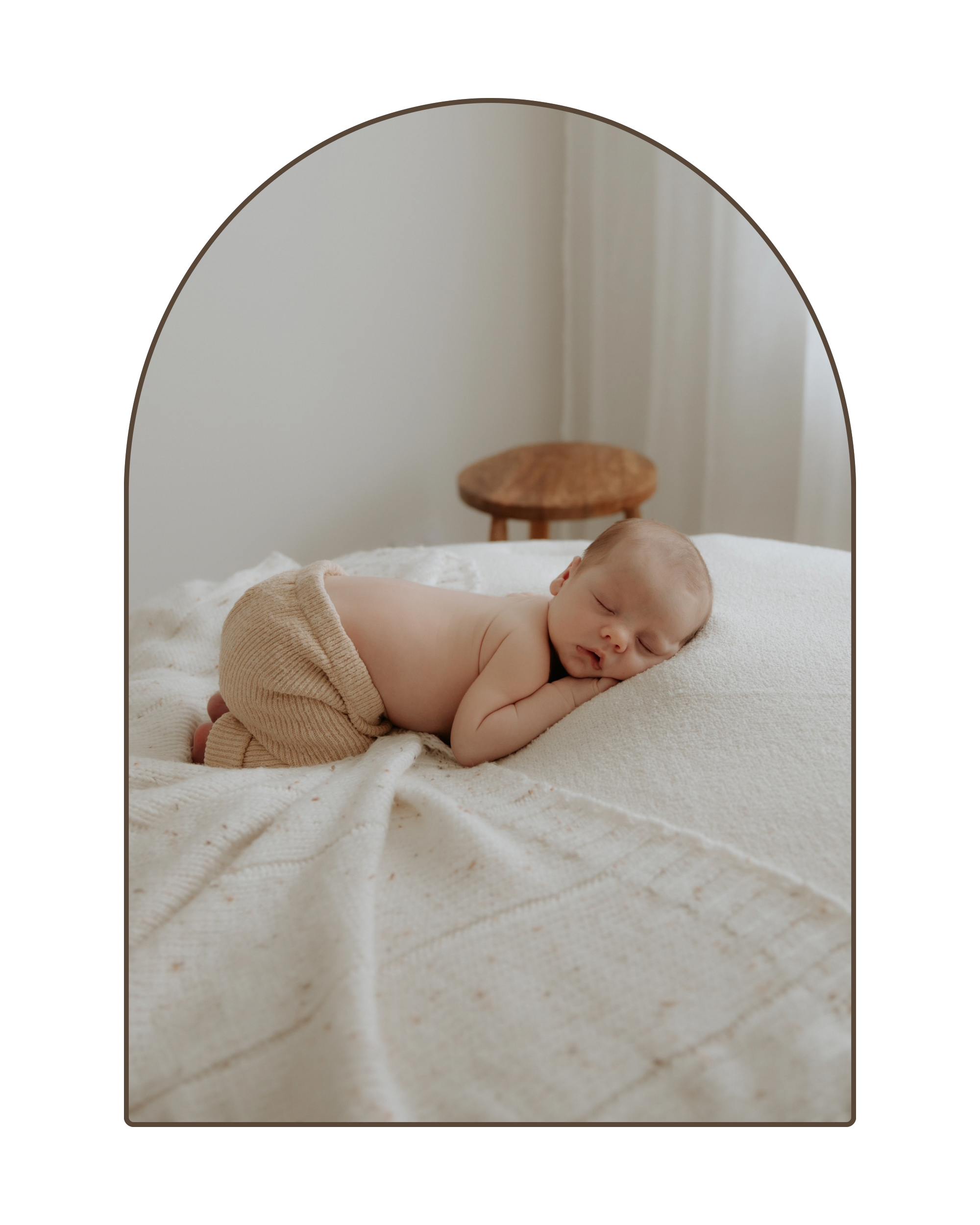 A sleeping baby lying on a cream-colored bed with a textured blanket, wearing beige knit shorts, and resting on their side with head on pillow.
