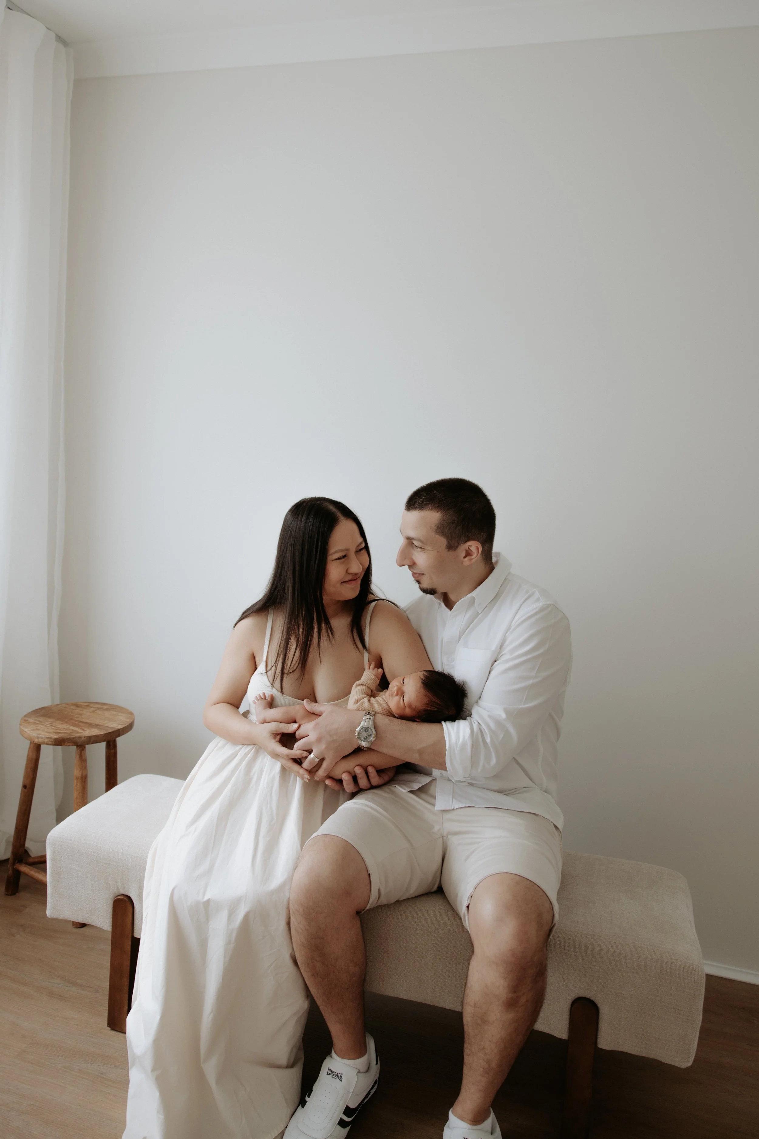 A happy family: mother, father, and their newborn baby sitting on a bench in a minimalist room, sharing a tender moment.