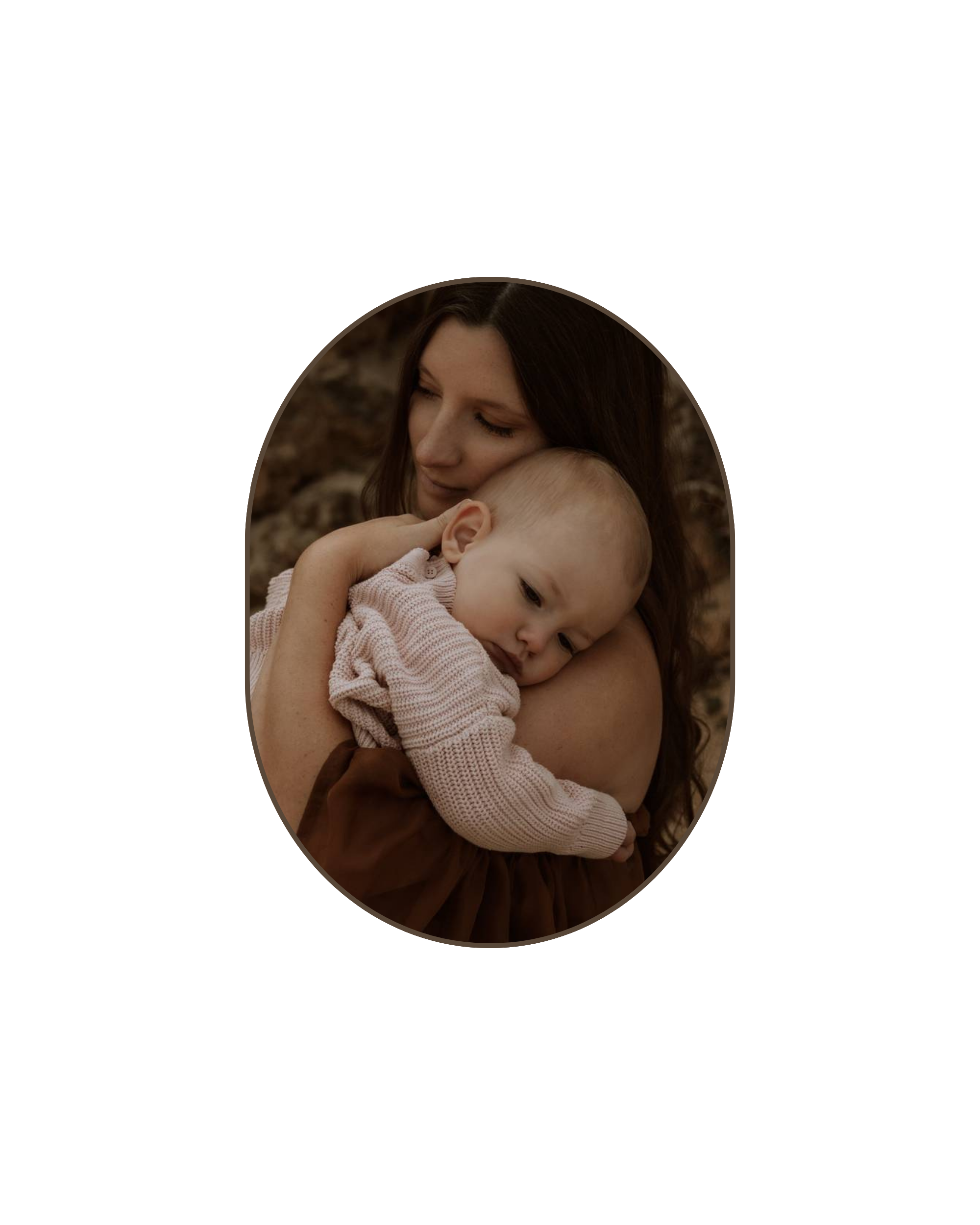A woman holding a young child close, with both appearing to be in a peaceful, reflective moment outdoors at a rocky beach in Perth.