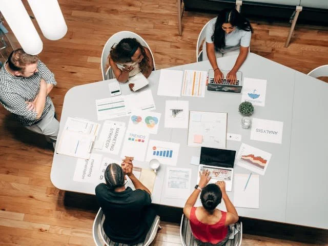 A team working on a marketing plan, with designs and laptops on the work table in front of them.