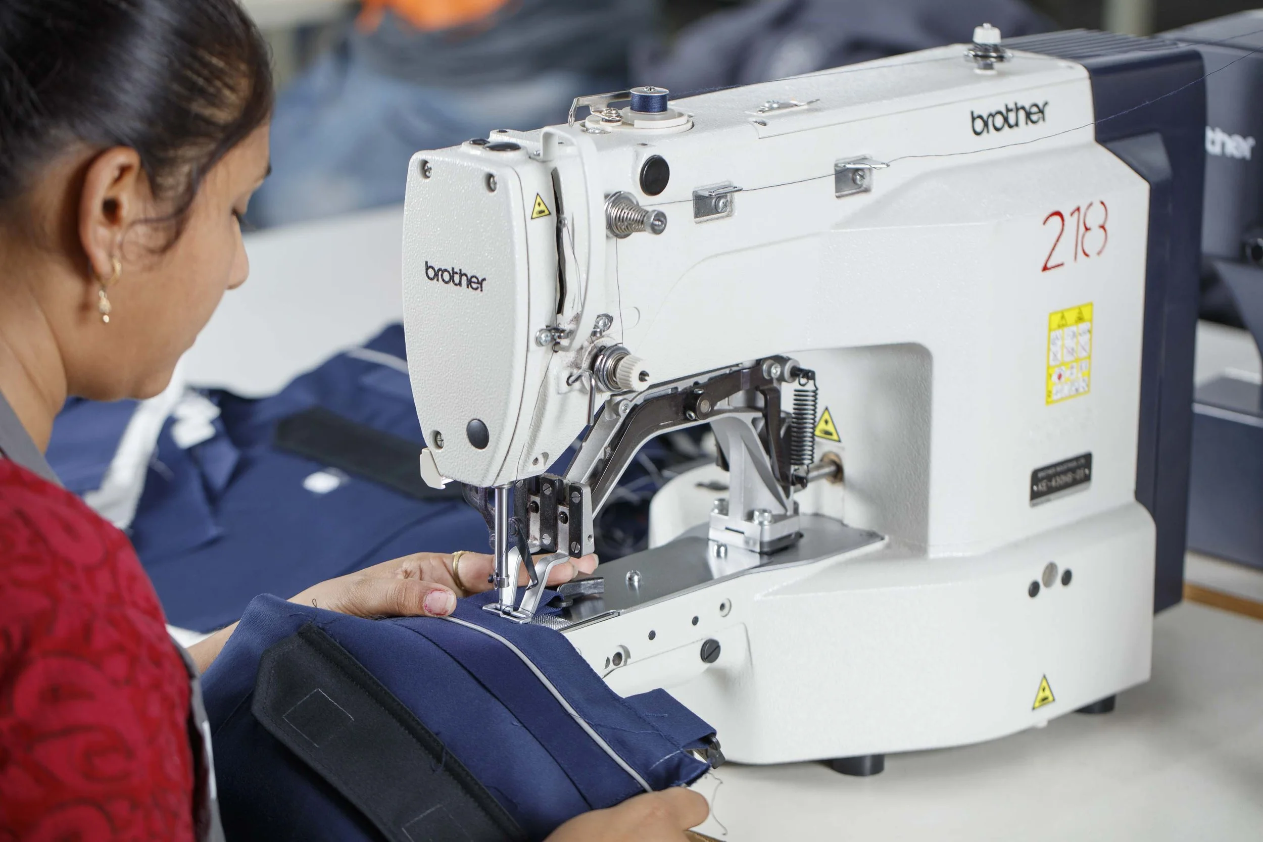 A woman operating a Brother industrial sewing machine stitching blue fabric.