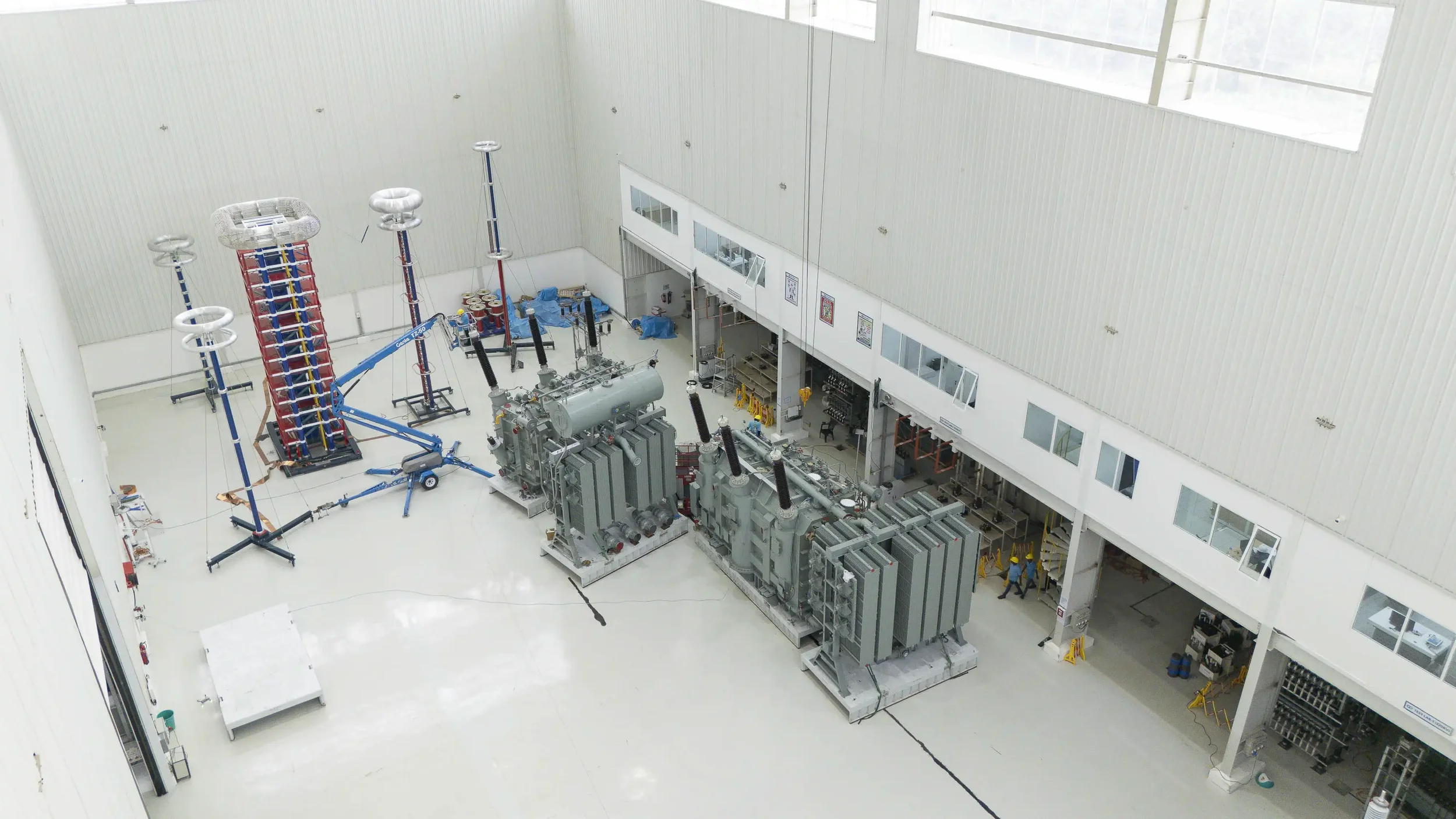 A wide-angle high-level perspective of the test lab containing two large transformer units and high-voltage testing rigs.