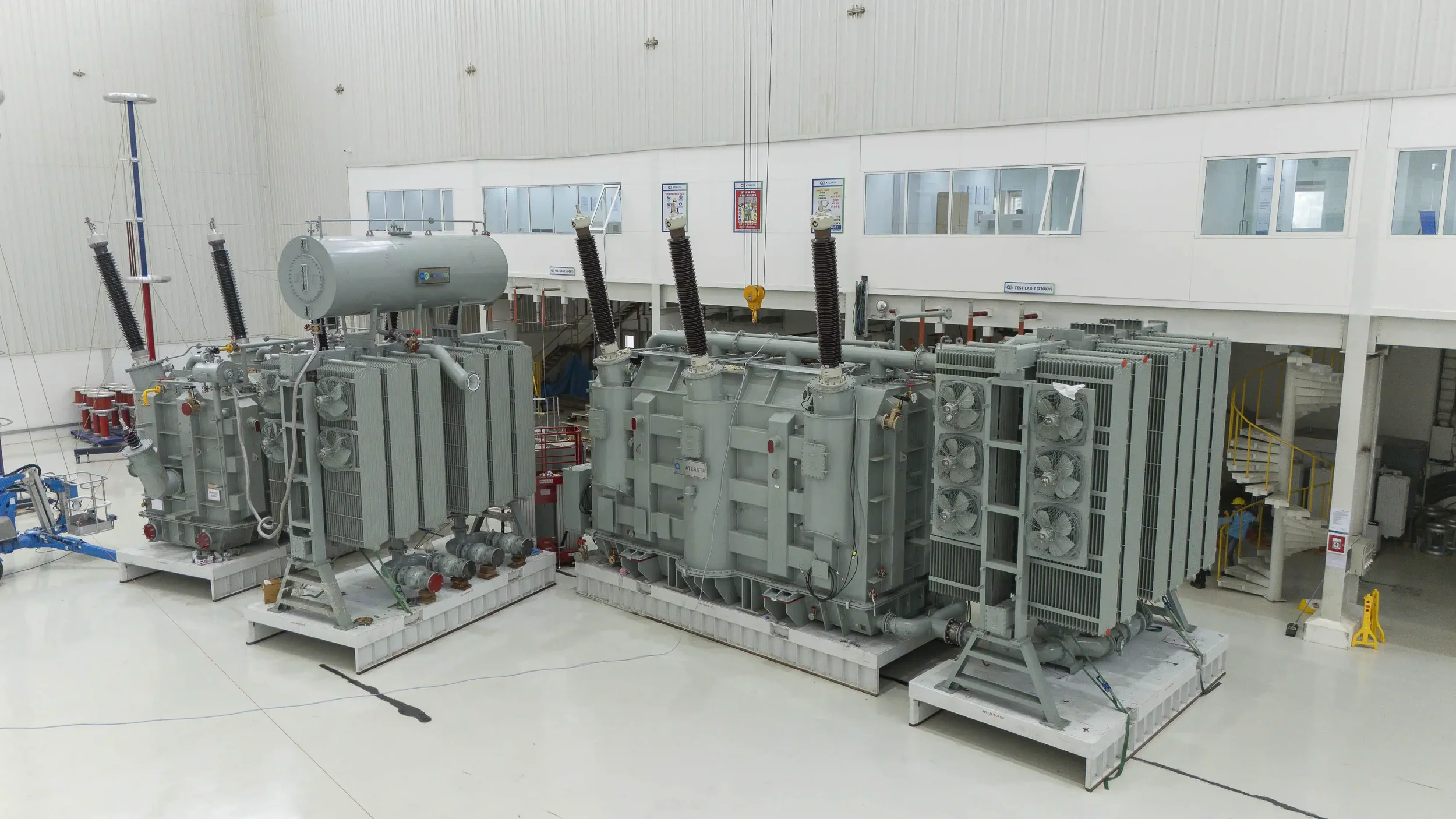 A clear, wide shot of two completed power transformers side-by-side in the facility testing hall