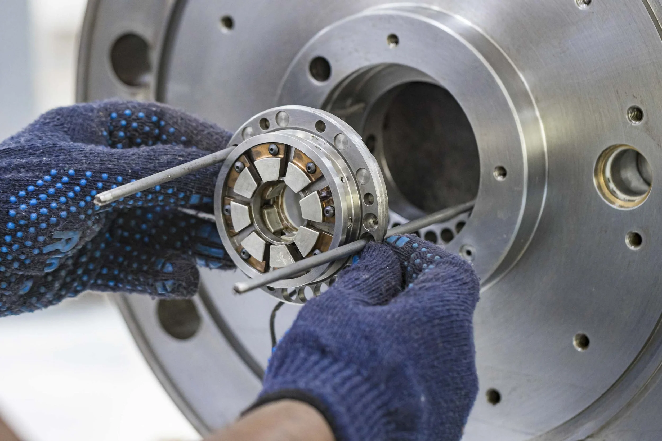 Technician in blue gloves assembling or repairing a small metallic component inside a large industrial machine or turbine.