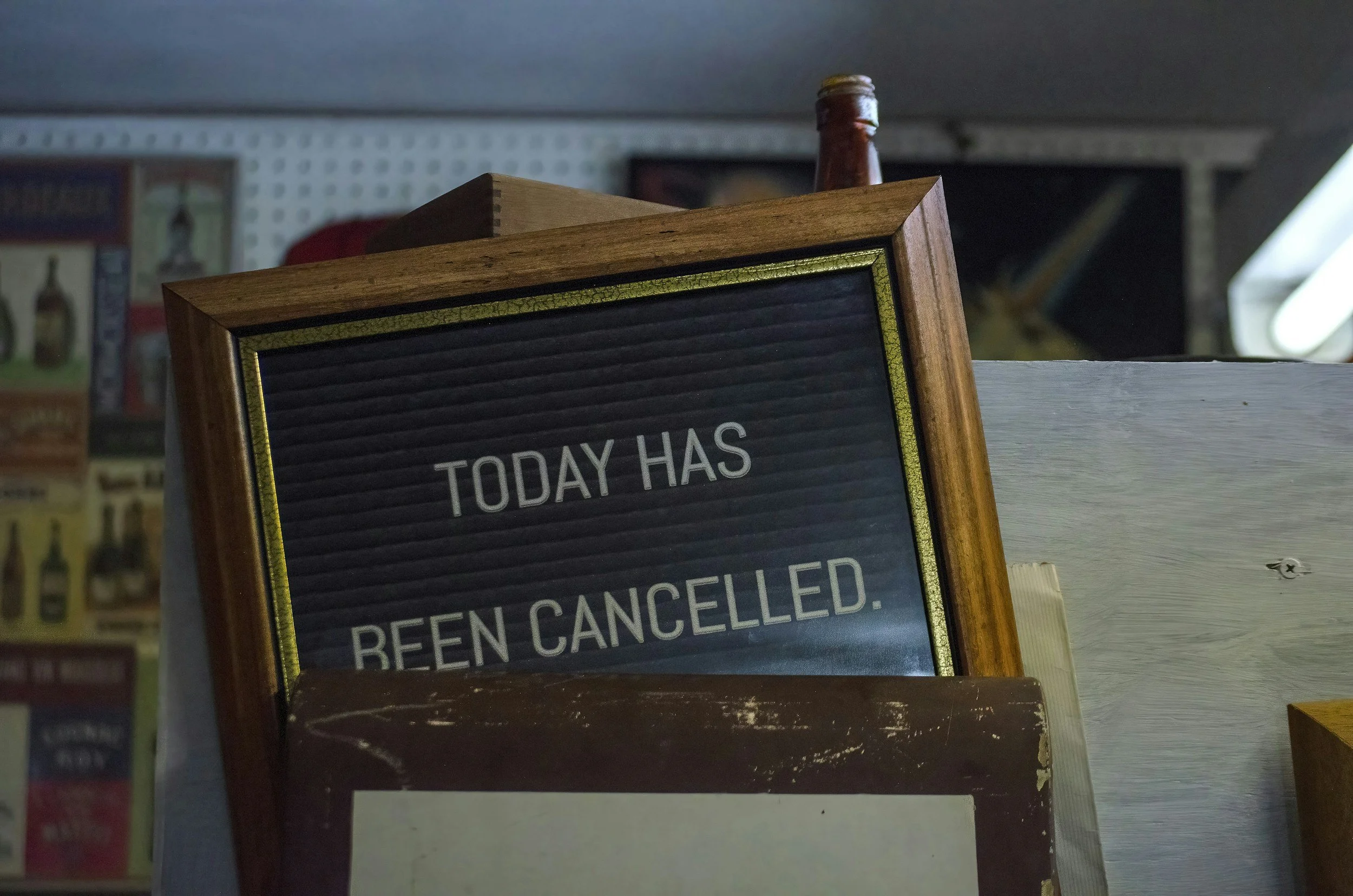 A sign with black background and white letters that reads 'Today Has Been Canceled' with a wooden frame, placed among other items in a store or cafe.