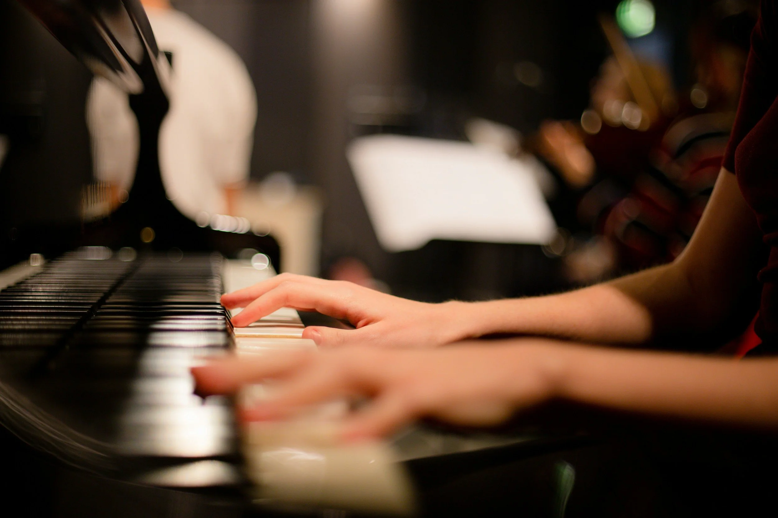 Close-up of a person's hands playing a black and white piano keyboard in a dimly lit room.