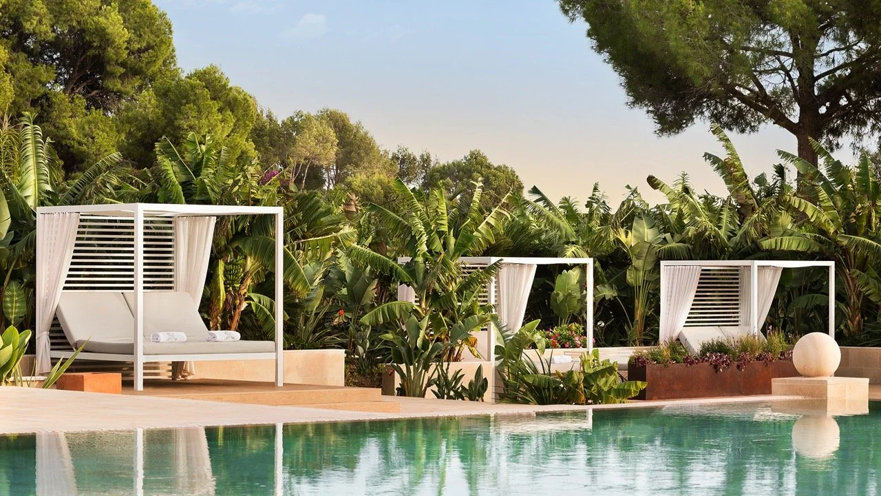 Luxury poolside lounging area with white cabanas and lush green tropical vegetation in the background.