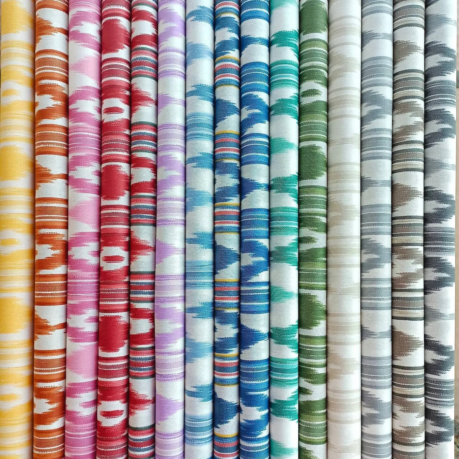 A row of rolled-up fabric with colorful, striped, and patterned designs, arranged in a range of colors from yellow to gray.