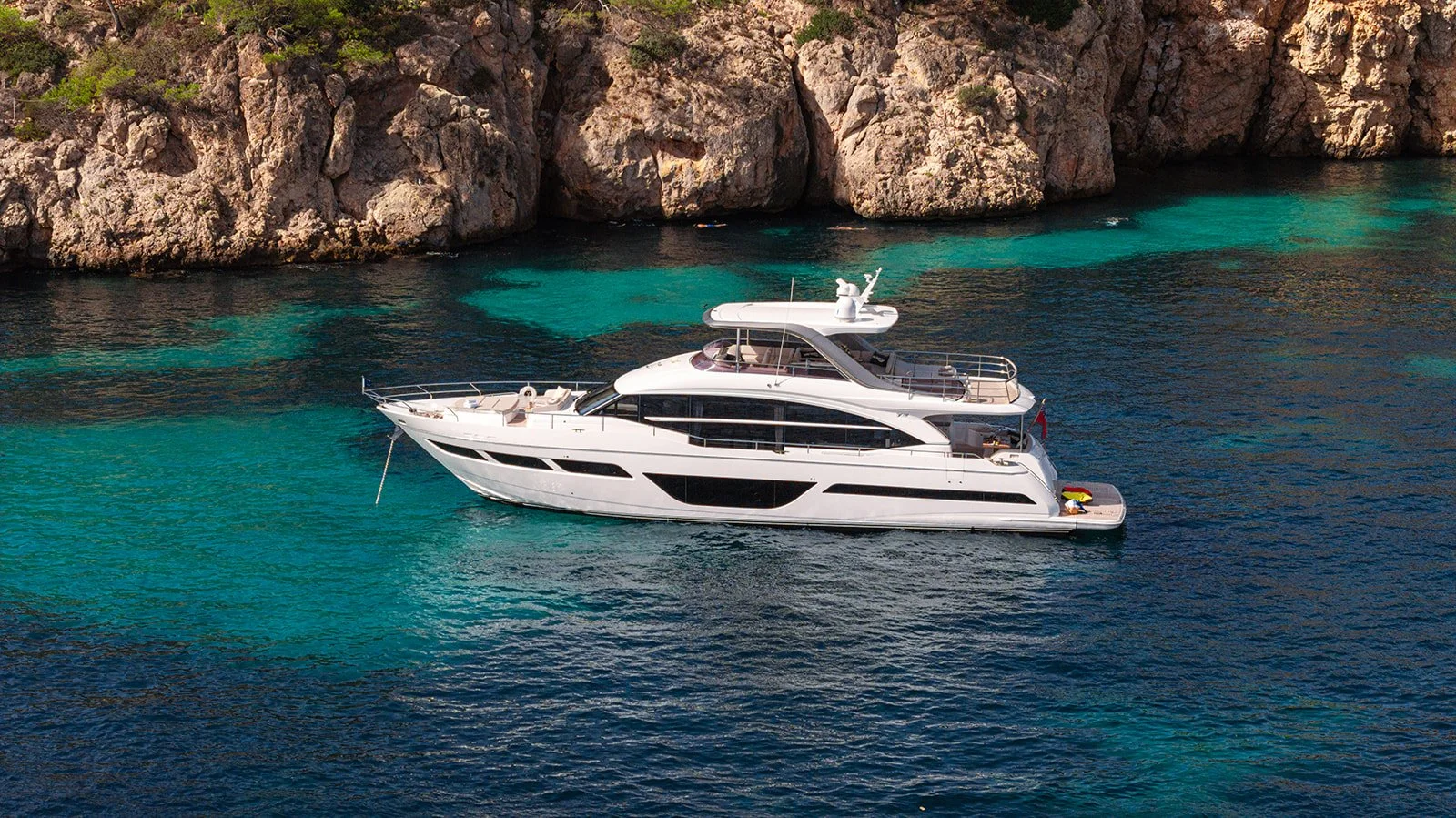 A large white yacht floating on clear blue water near a rocky island with green vegetation.