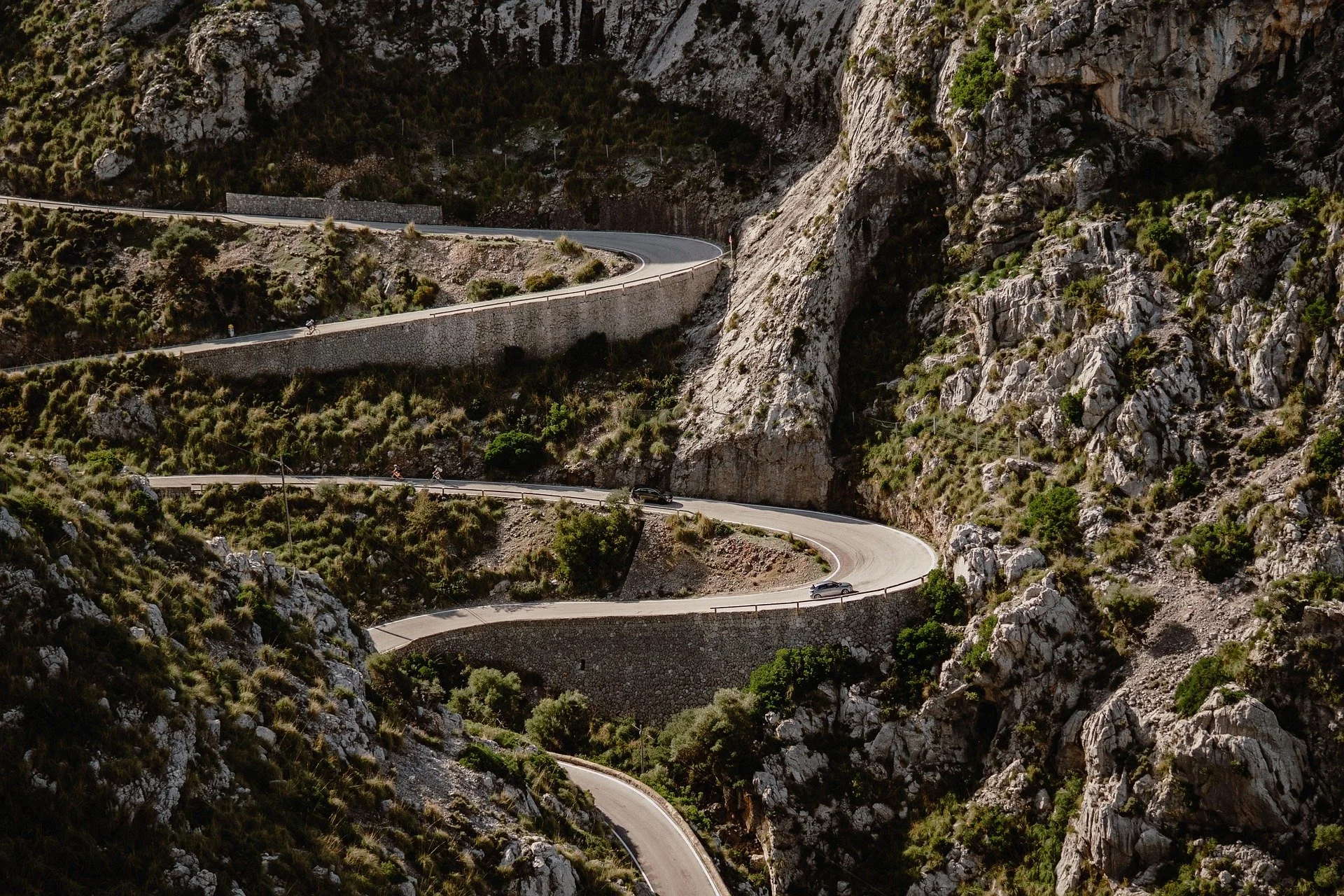 A winding mountain road with sharp turns, cutting through a rocky, green landscape.