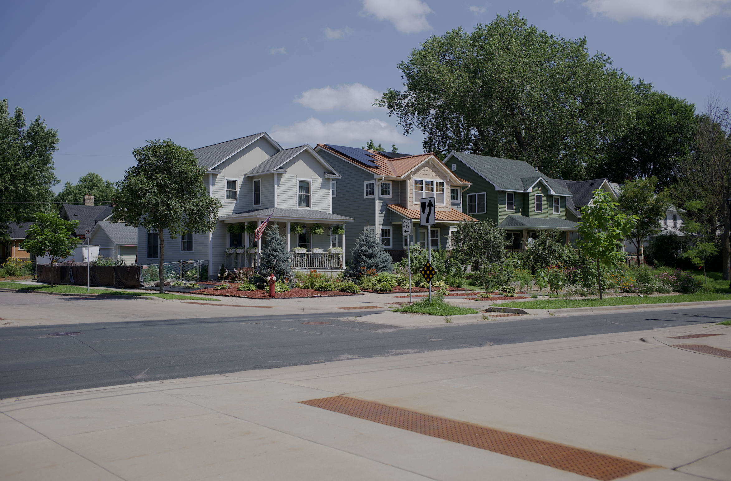 Image of three houses on city street block with landscaping and trees on a sunny day on a boulevard.
