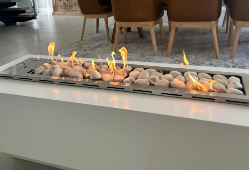 Modern indoor fireplace with burning flames, set on a white surface in a room with brown chairs and a carpet.