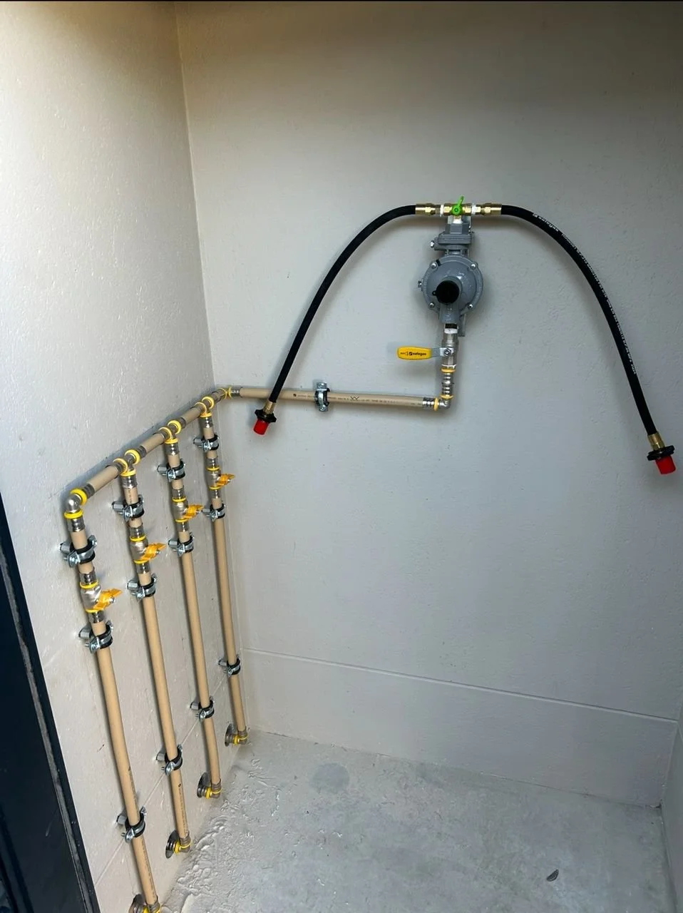 LP Gas changeover system with multiple beige pipes connected with yellow valves on a beige wall, and a control valve with black hoses attached.