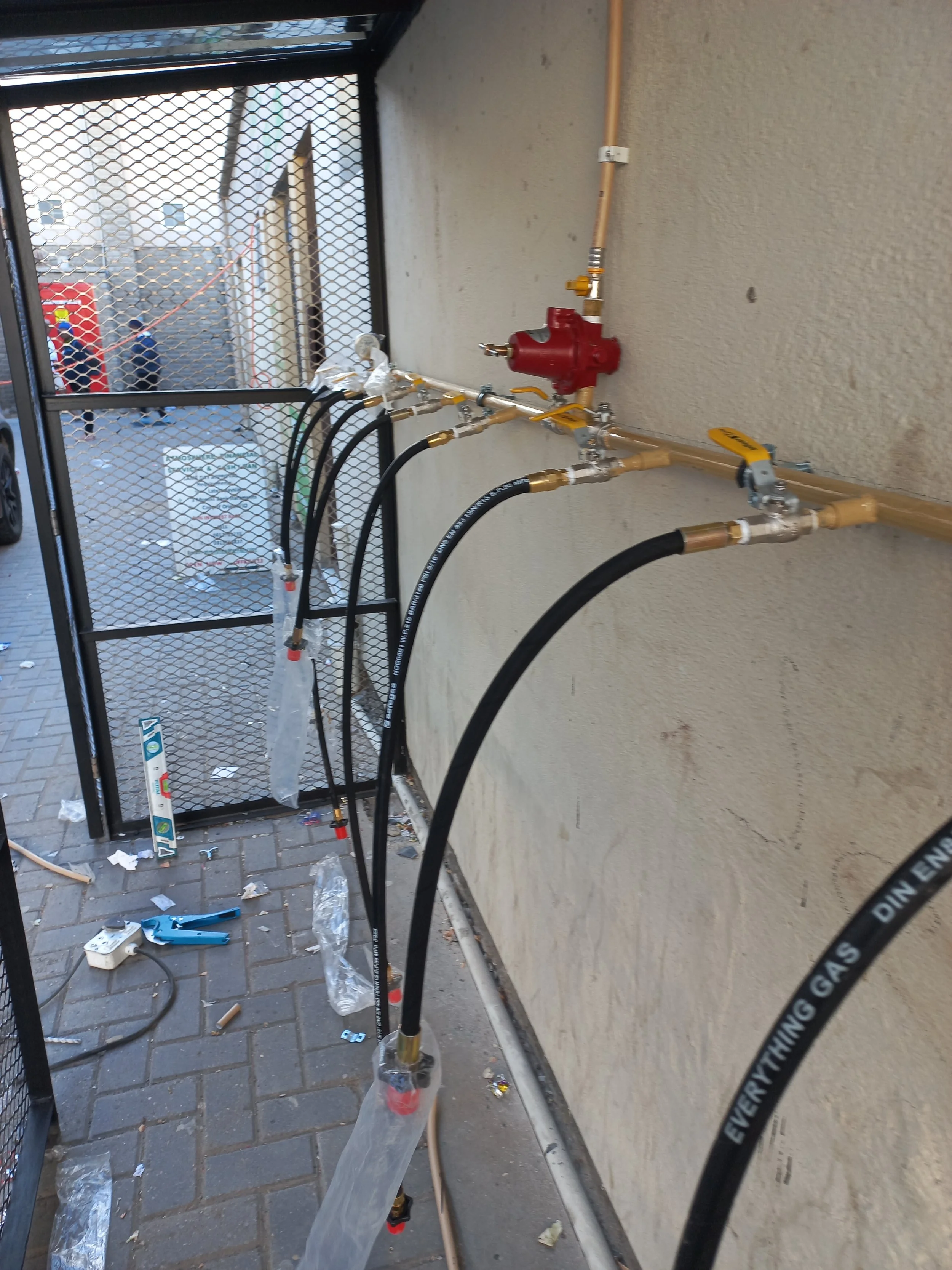 Gas piping system installed along a wall with black hoses, valves, and a red pressure regulator.