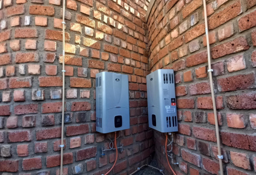 Two gray outdoor LP Gas water heater units installed in a brick corner.