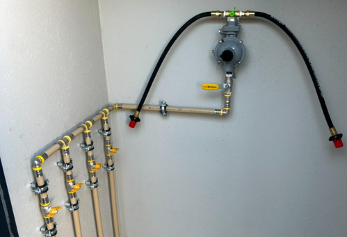 LP Gas changeover system with pipes, valves, and a pressure regulator attached to a wall.