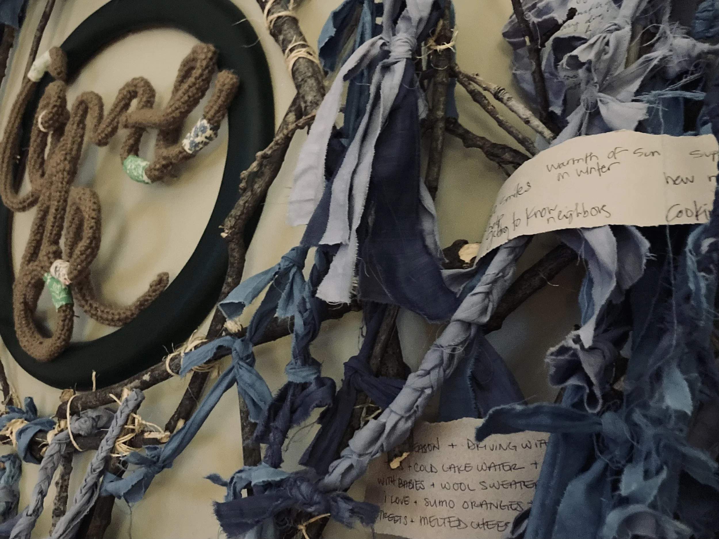 The image shows a collection of fabric scraps, branches, and a carved ring with beads. There is also handwritten notes visible on a piece of paper.