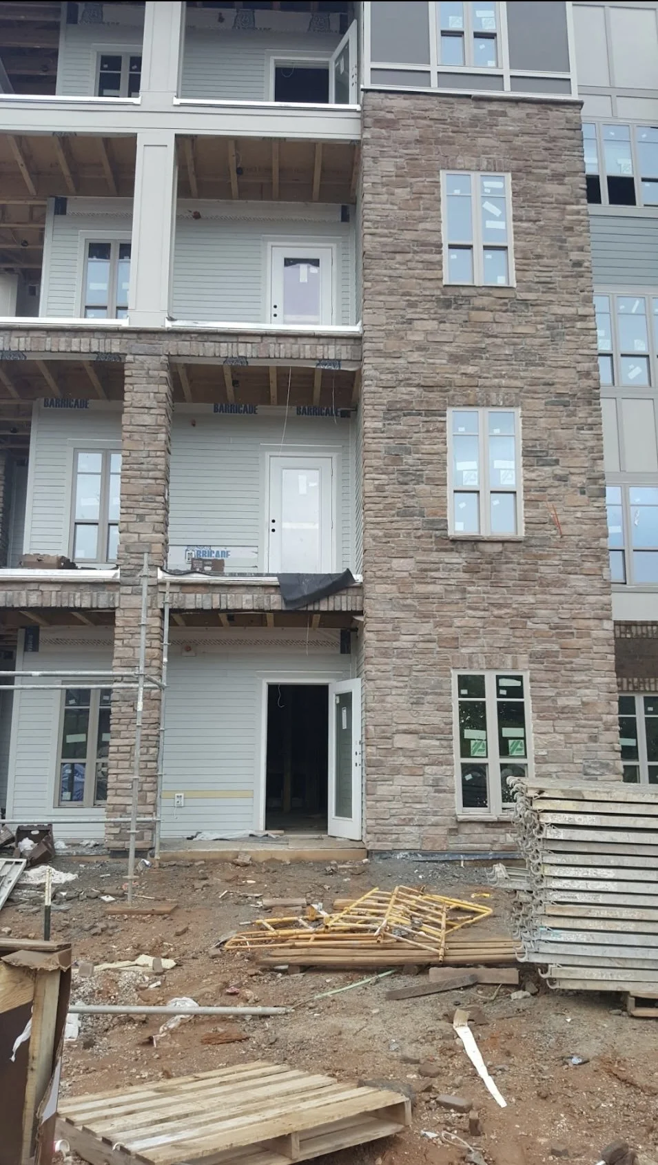Under construction multi-story residential building with brick and siding exterior, windows, and scaffolding, with construction materials and dirt in the foreground.