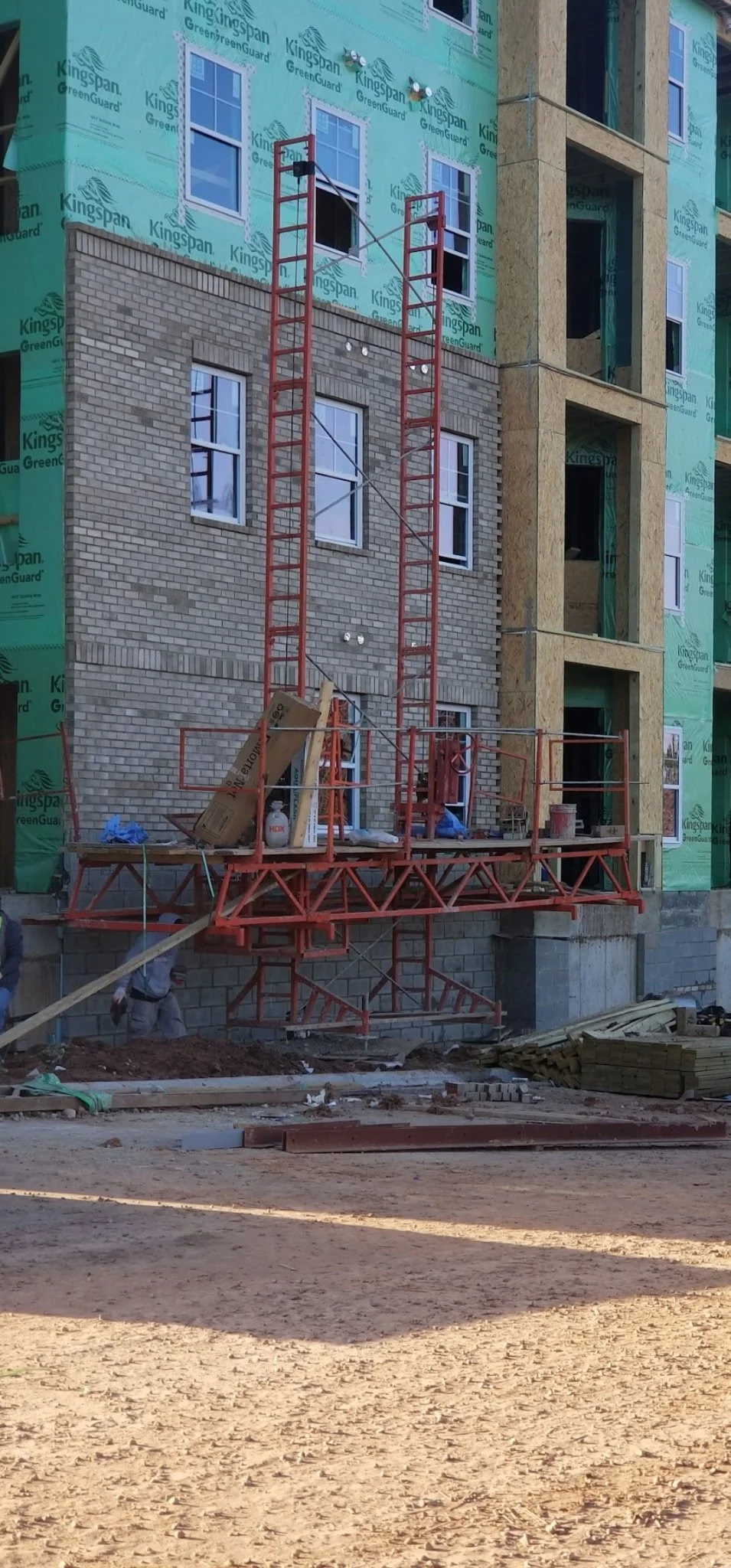 Construction site with partially built multi-story building, scaffolding, and construction materials on ground