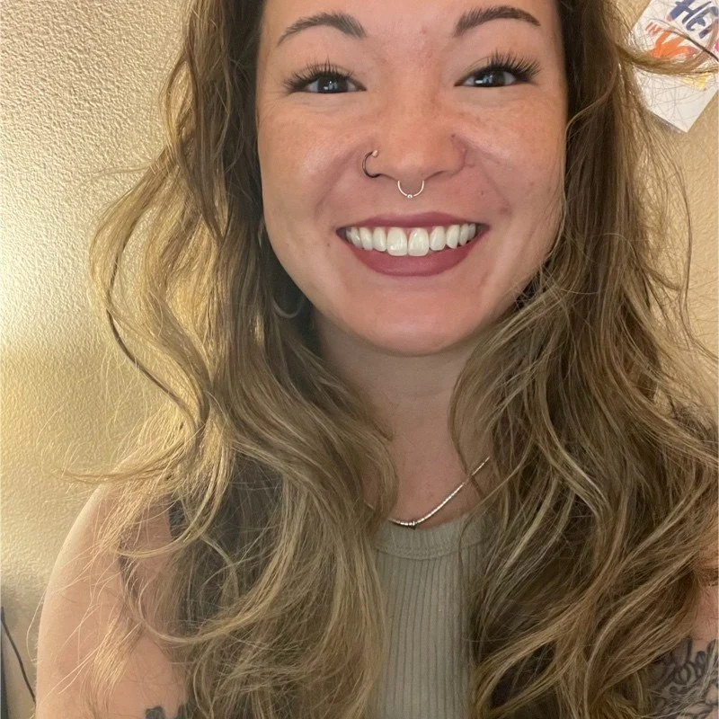 Leona Martinez, a woman with long wavy brown hair and two silver nose rings, looking at the camera with a wide smile.