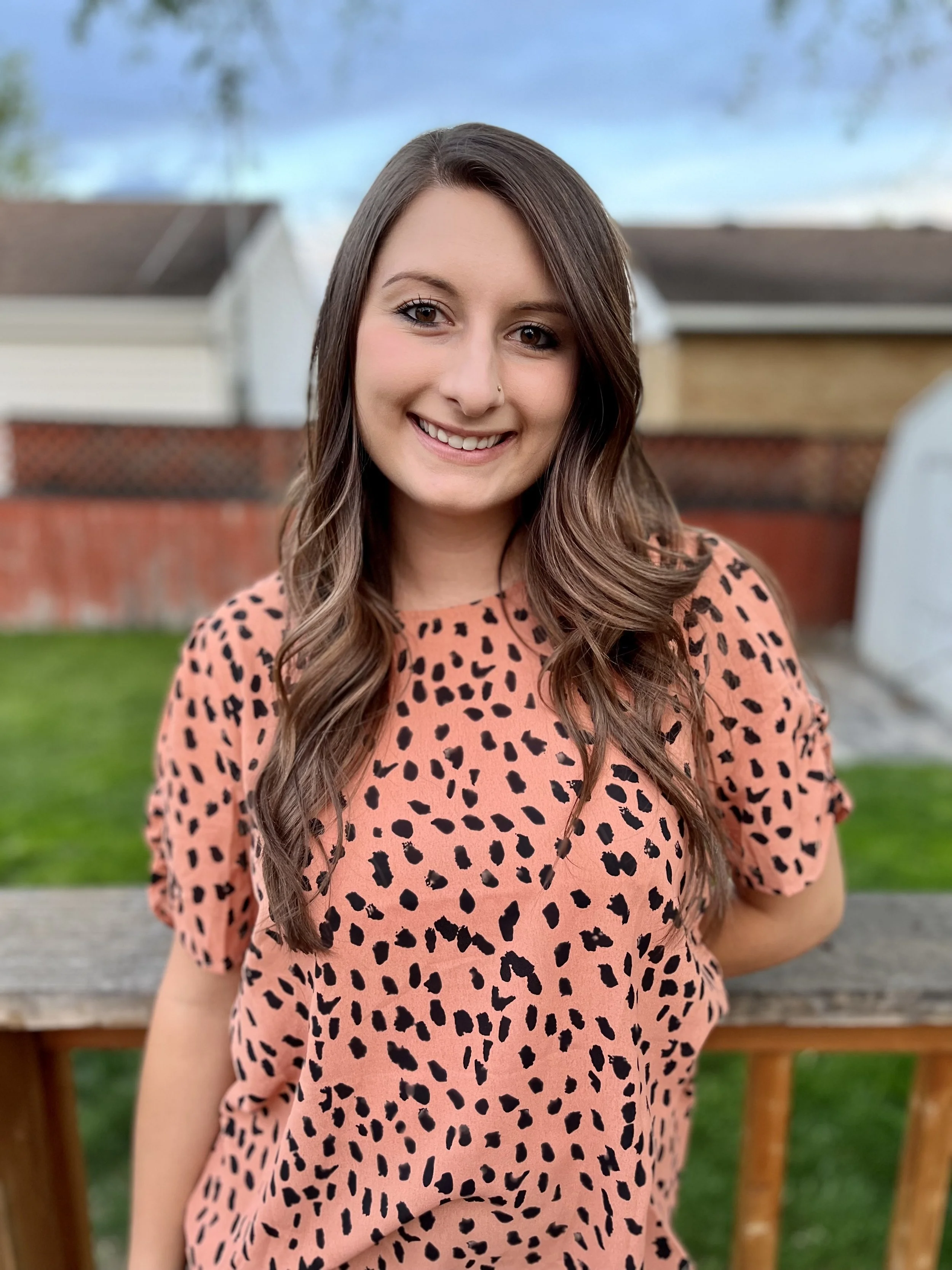 Emma Fitzpatrick, a woman with long wavy brown hair smiling at the camera and wearing a pink spotted top. 