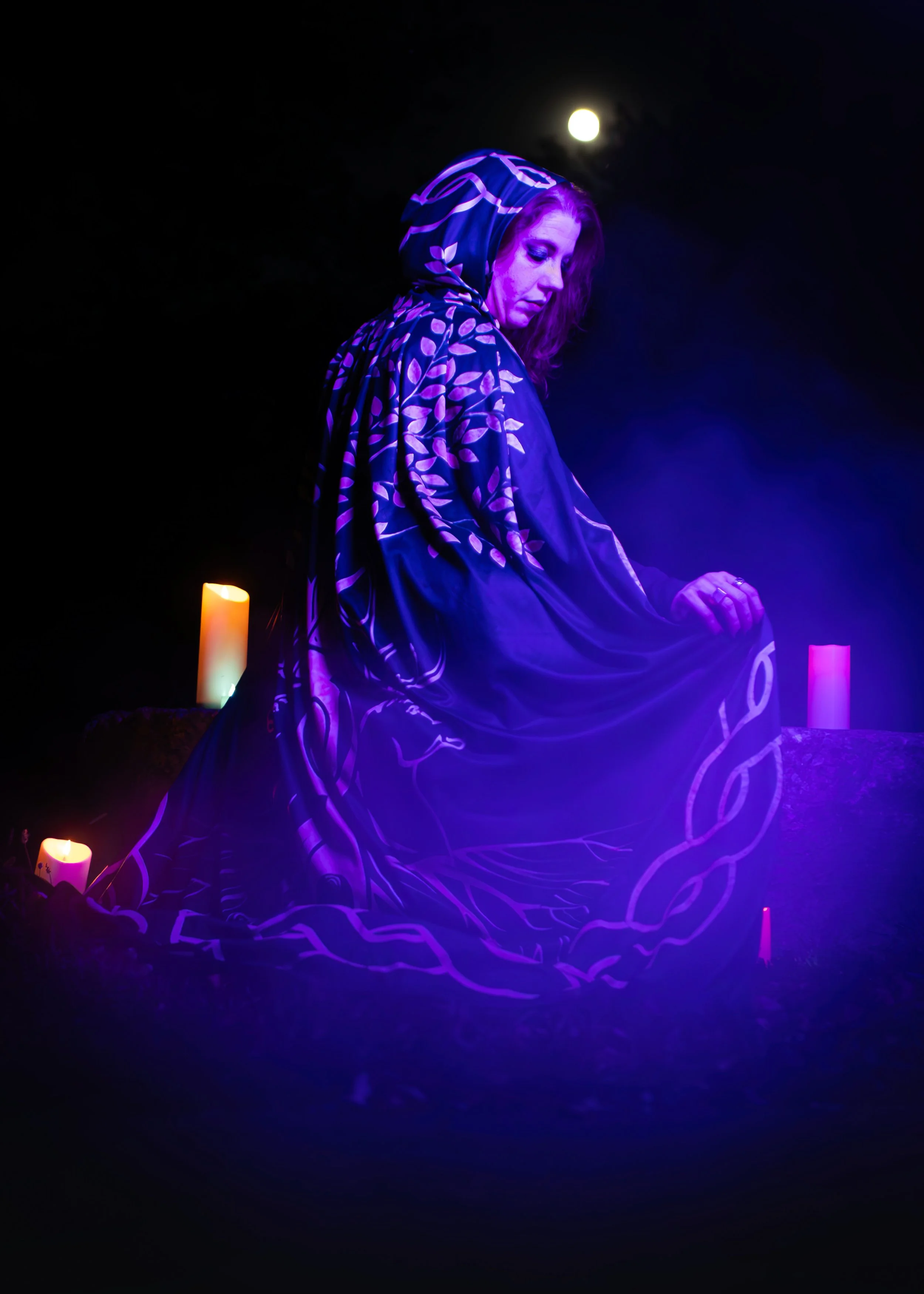 woman sitting in a cloak surrounded by candles