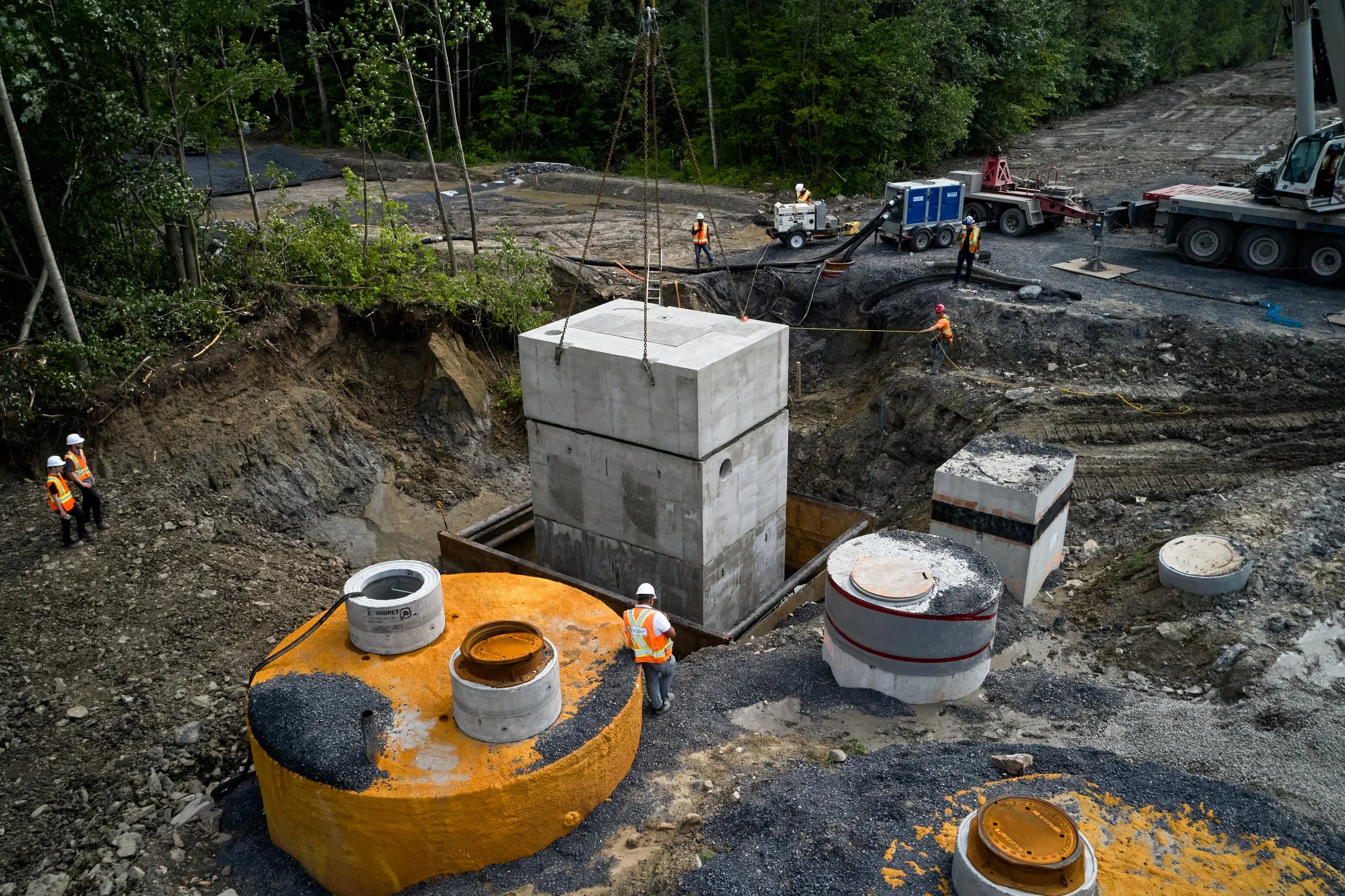 Chantier de construction avec des ouvriers portant des casques, excavatrices, et divers éléments de structure en béton.