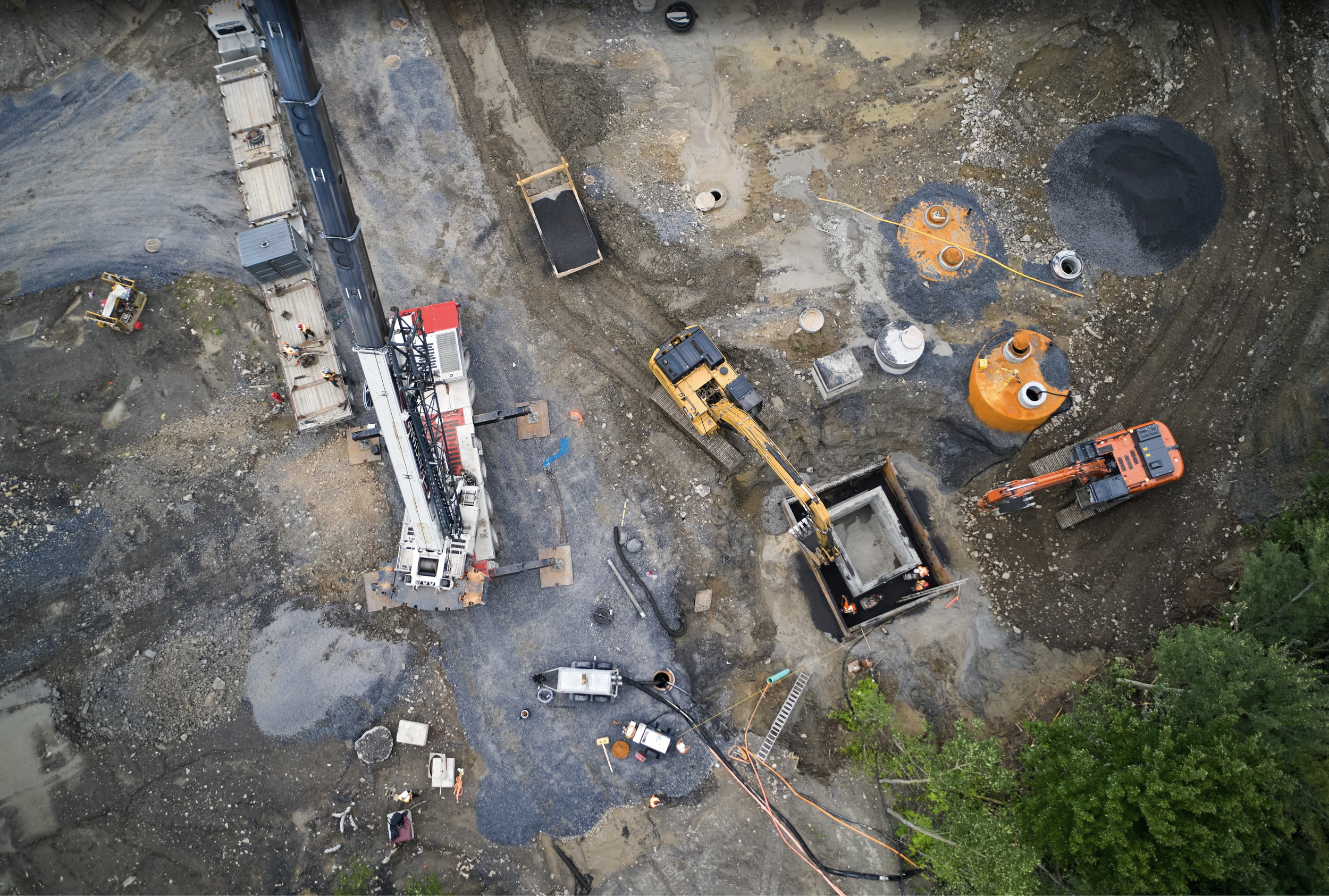 Vue aérienne d'un chantier de construction avec des camions, des excavatrices et des ouvriers travaillant sur le terrain.