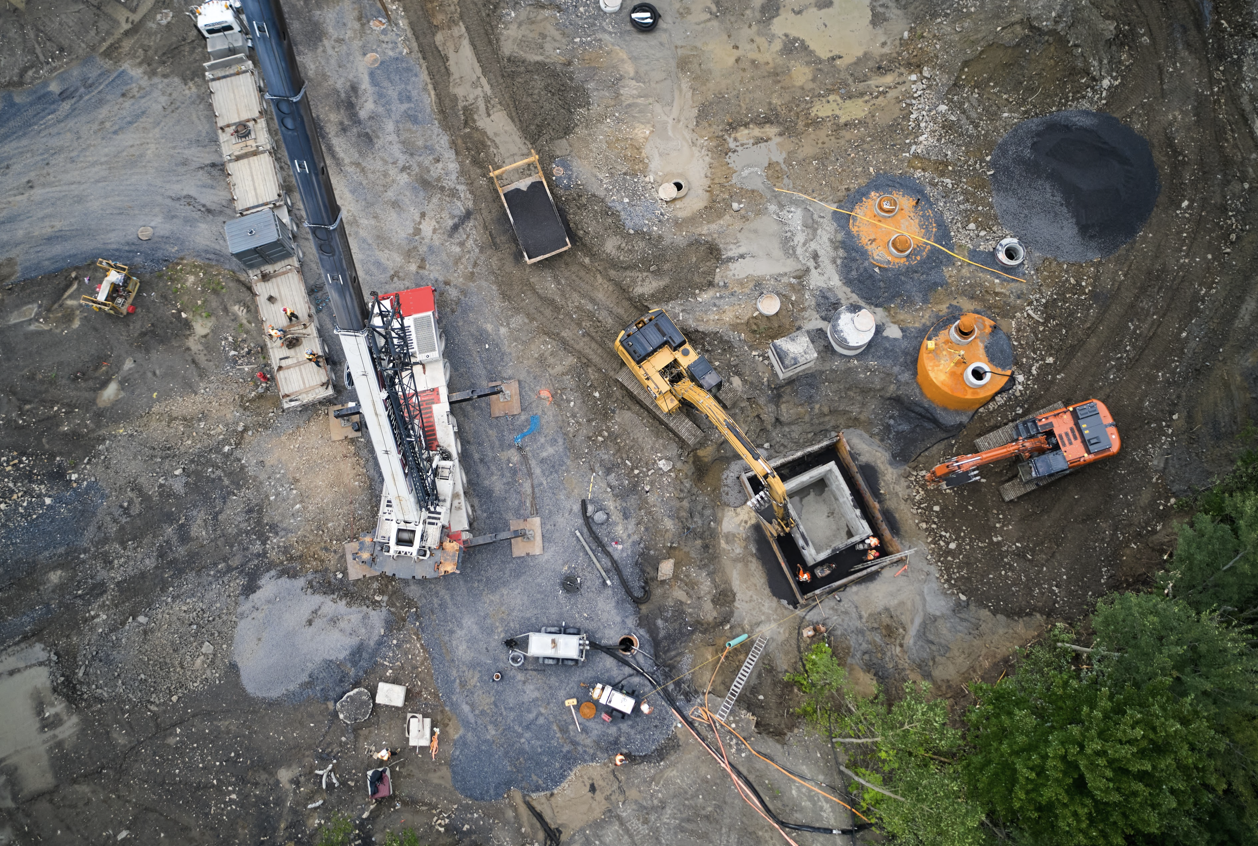 Vue aérienne d'un site de construction avec machines excavatrices, tuyaux, et zones excavées.