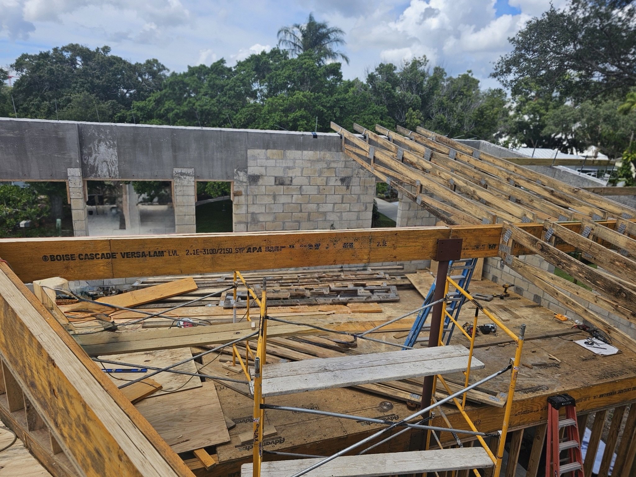 Residential construction site with wooden framework, scaffolding, and building materials in progress under a partly cloudy sky.