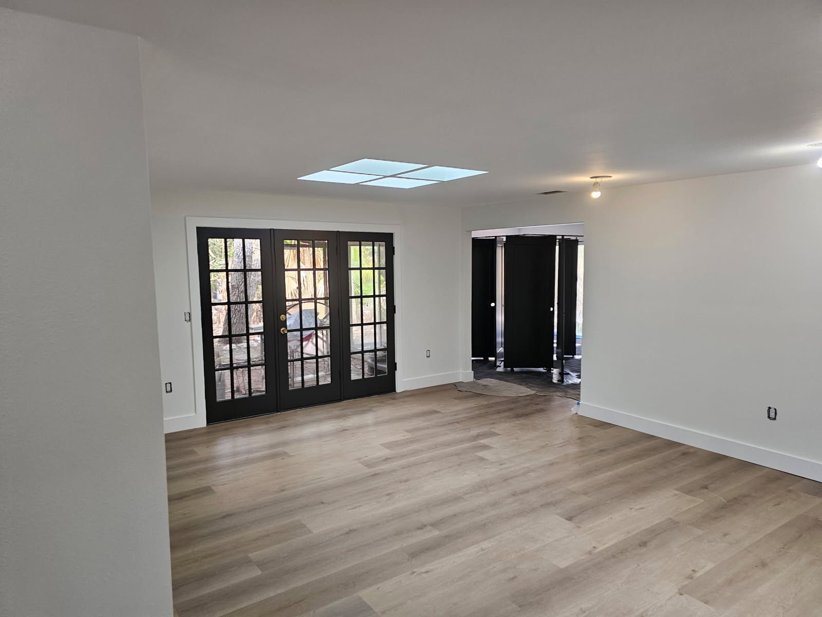 Empty room with wooden flooring, black-framed French doors, recessed lighting, and a skylight.